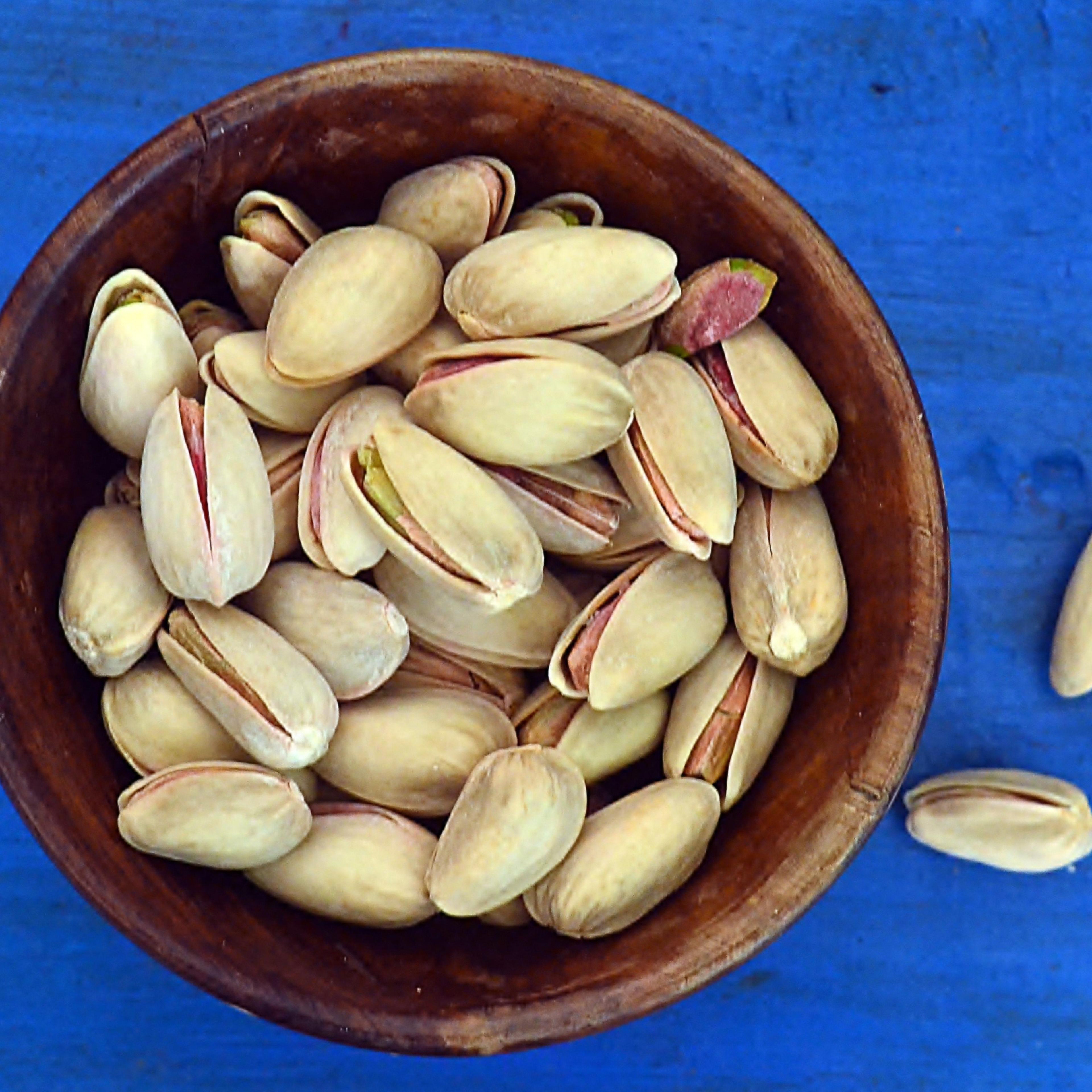 Pistachio nuts in a wooden bowl against blue background