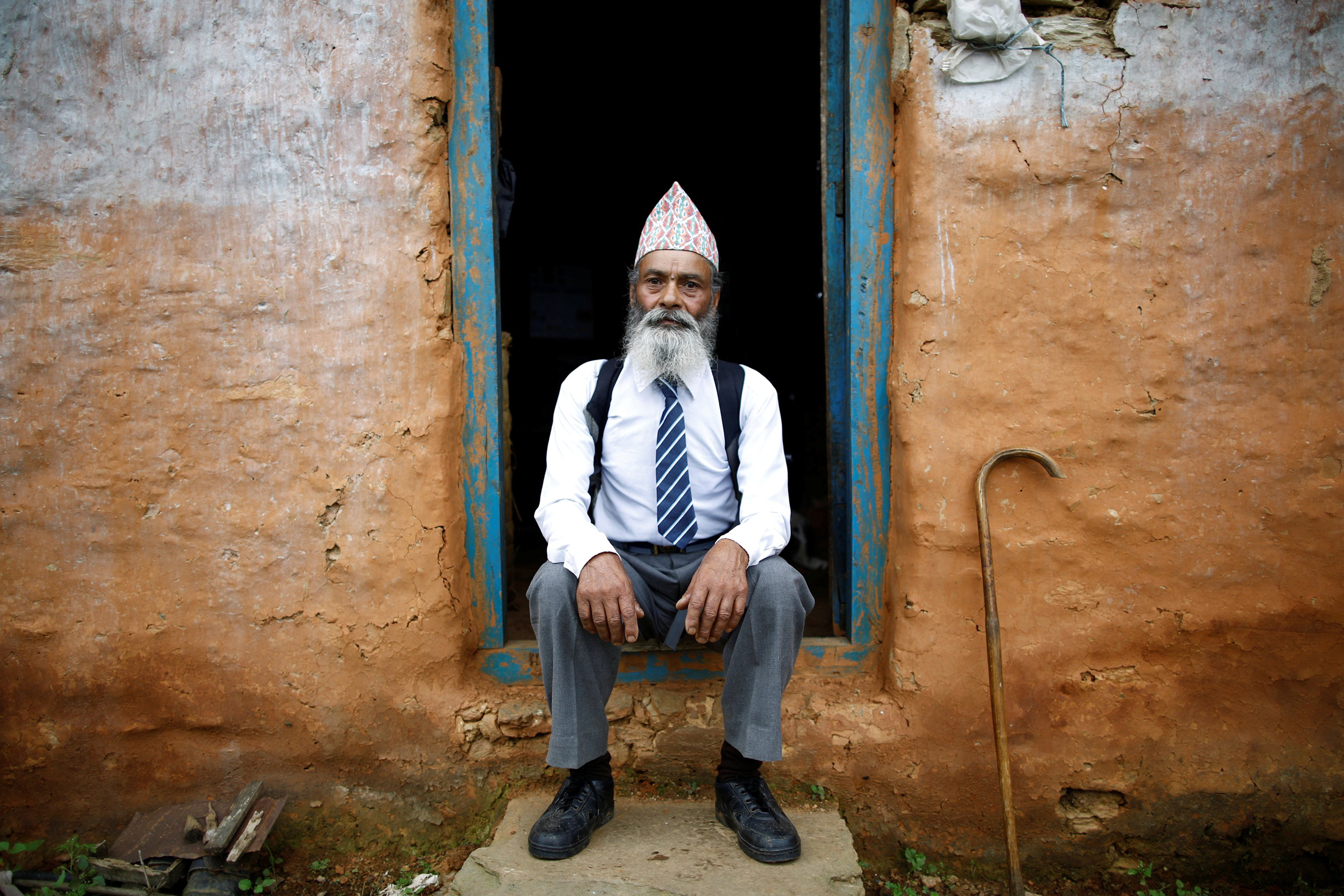 Durga Kami, 68, who is studying tenth grade at Shree Kala Bhairab Higher Secondary School, poses for a picture wearing his school uniform at the door of his one-room house in Syangja, Nepal, June 5, 2016. REUTERS/Navesh Chitrakar. SEARCH "DURGA KAMI" FOR