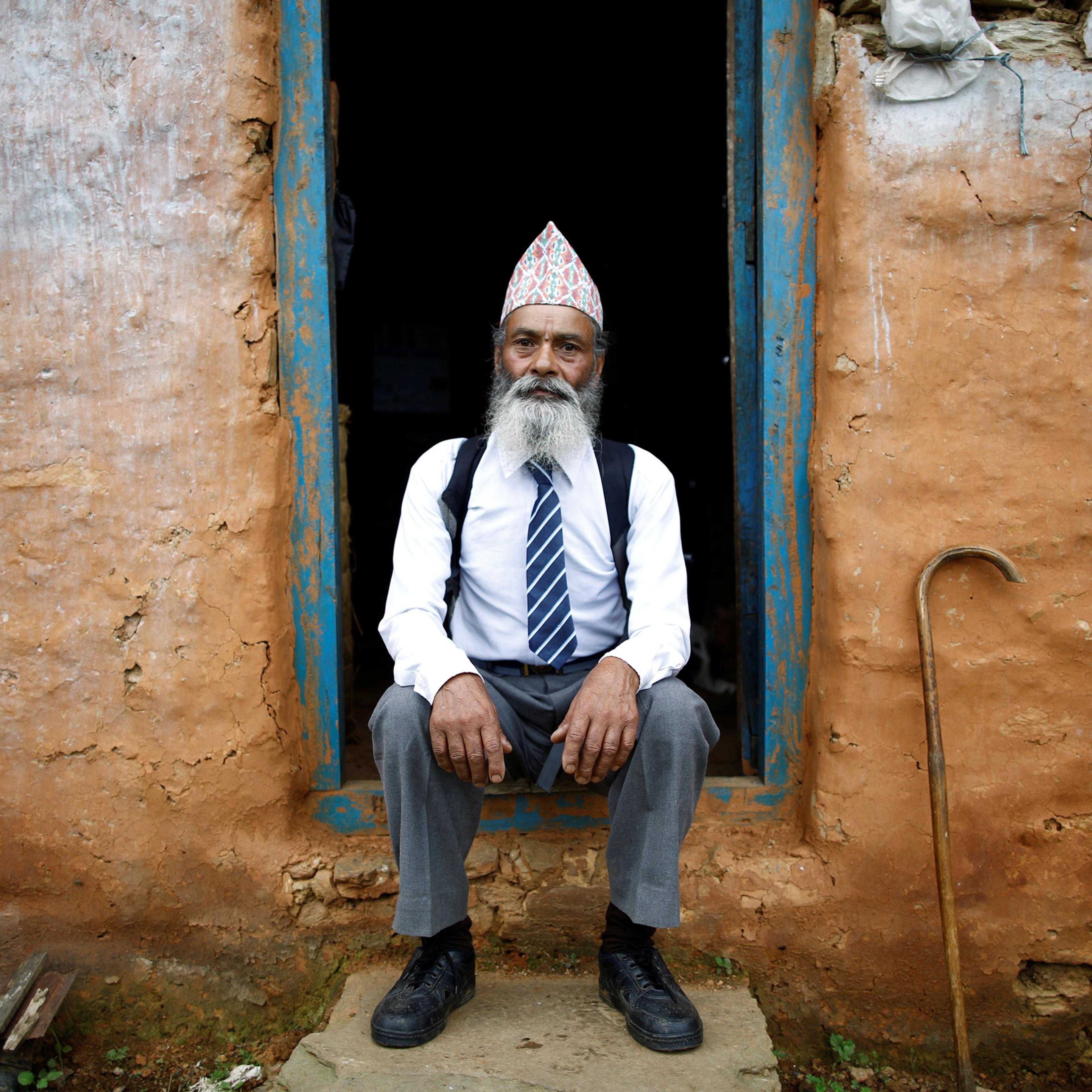 Durga Kami, 68, who is studying tenth grade at Shree Kala Bhairab Higher Secondary School, poses for a picture wearing his school uniform at the door of his one-room house in Syangja, Nepal, June 5, 2016. REUTERS/Navesh Chitrakar. SEARCH "DURGA KAMI" FOR