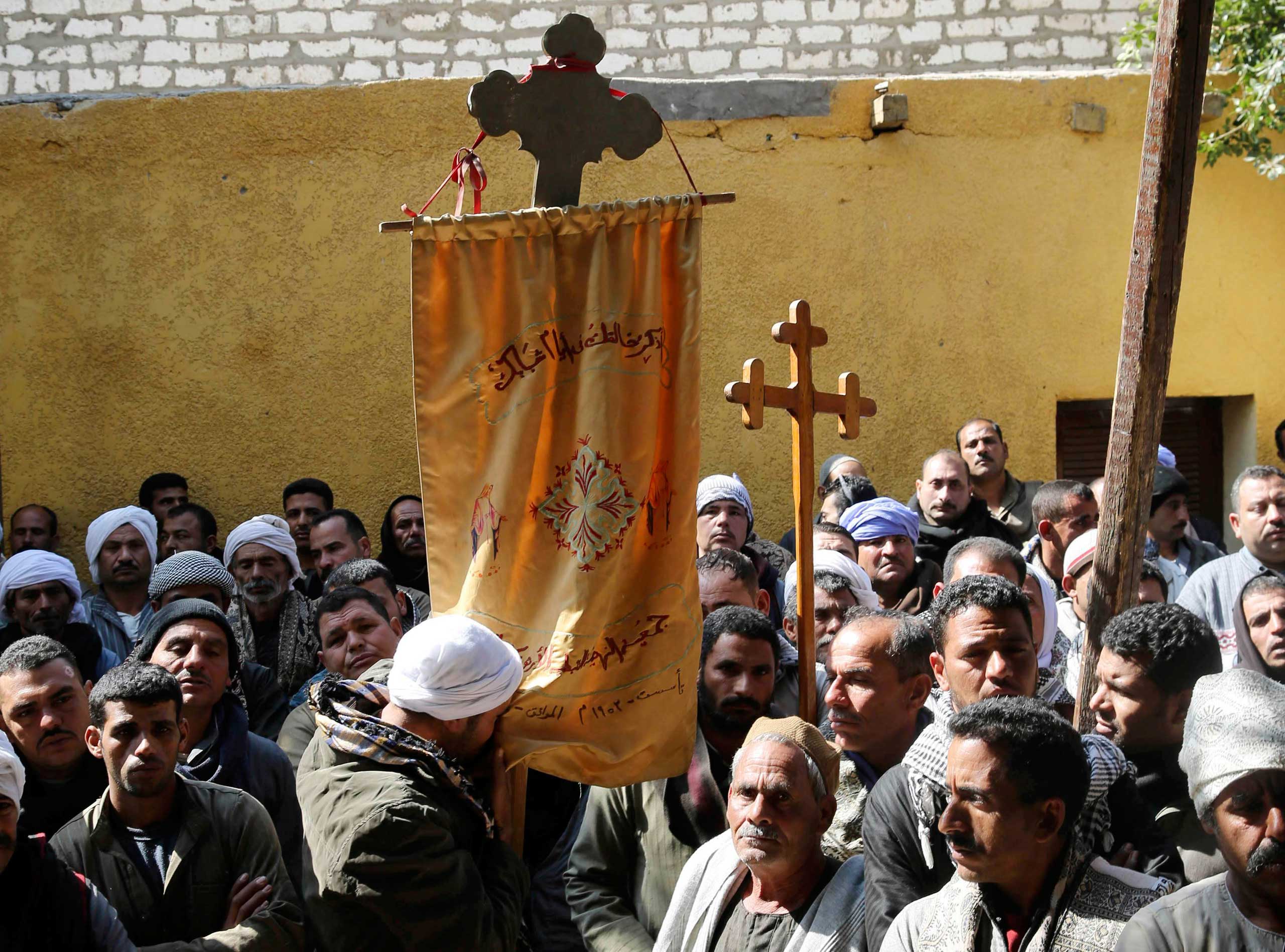 A Coptic man kisses a prayer banner, which is hung on a cross, as neighbors and friends of the relatives of Egyptian Coptic men who were killed in Libya stand at the courtyard of a church before attending a mass in El-Our village, in Minya governorate, s