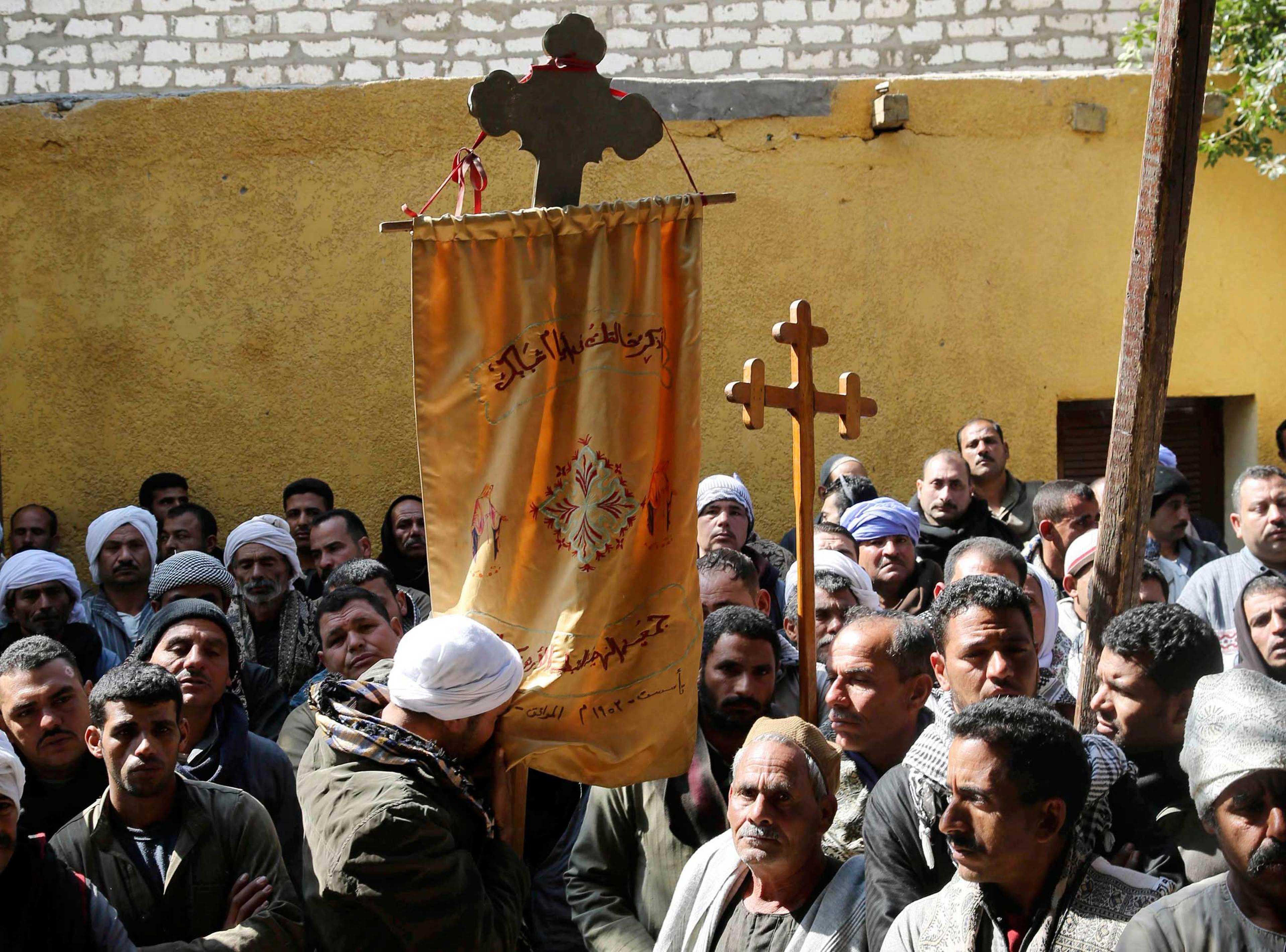 A Coptic man kisses a prayer banner, which is hung on a cross, as neighbors and friends of the relatives of Egyptian Coptic men who were killed in Libya stand at the courtyard of a church before attending a mass in El-Our village, in Minya governorate, s