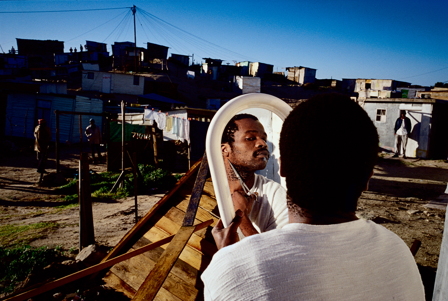 A mans cuts his beard outside his home in Khayelitsha, the biggest black township outside, Cape Town, South Africa, 2002.