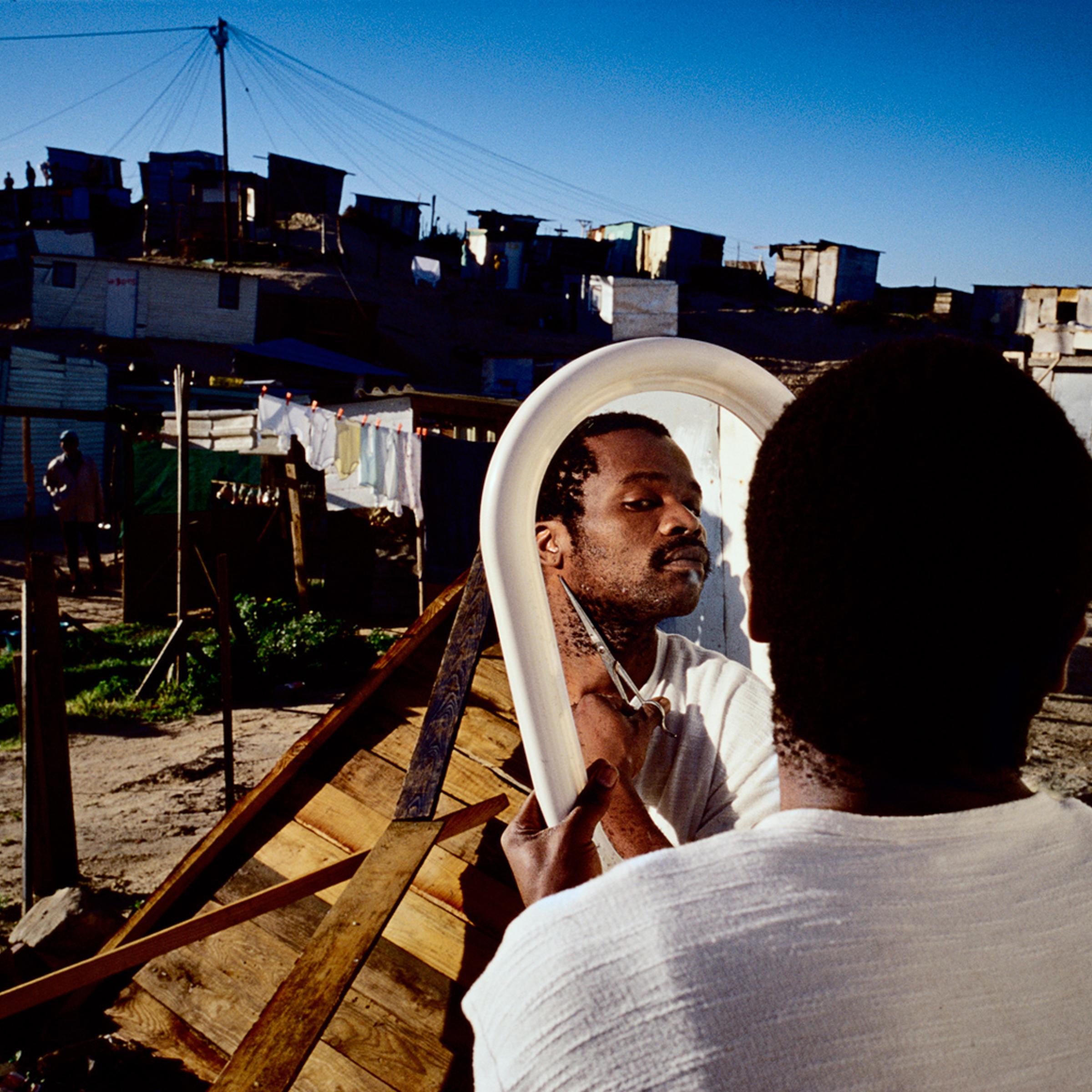 A mans cuts his beard outside his home in Khayelitsha, the biggest black township outside, Cape Town, South Africa, 2002.
