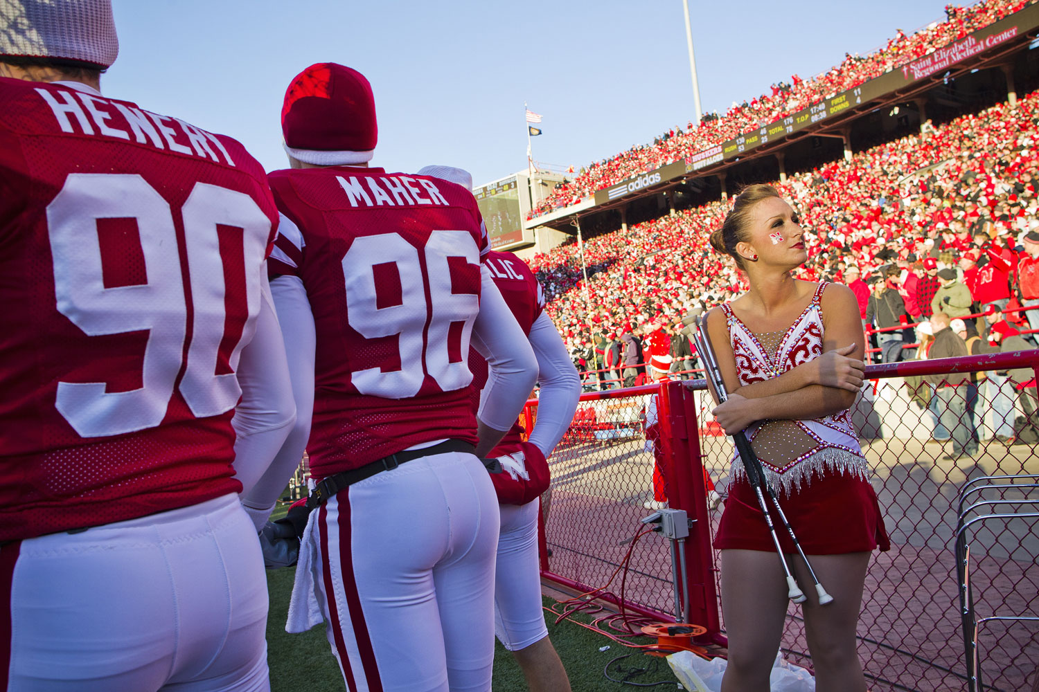 Nebraskaʼs baton twirler Rachel Foehlinger seeks warmth from a heater on the sidelines next to kickers Alex Henery and Brett Maher during a November 2010 game against Colorado. 