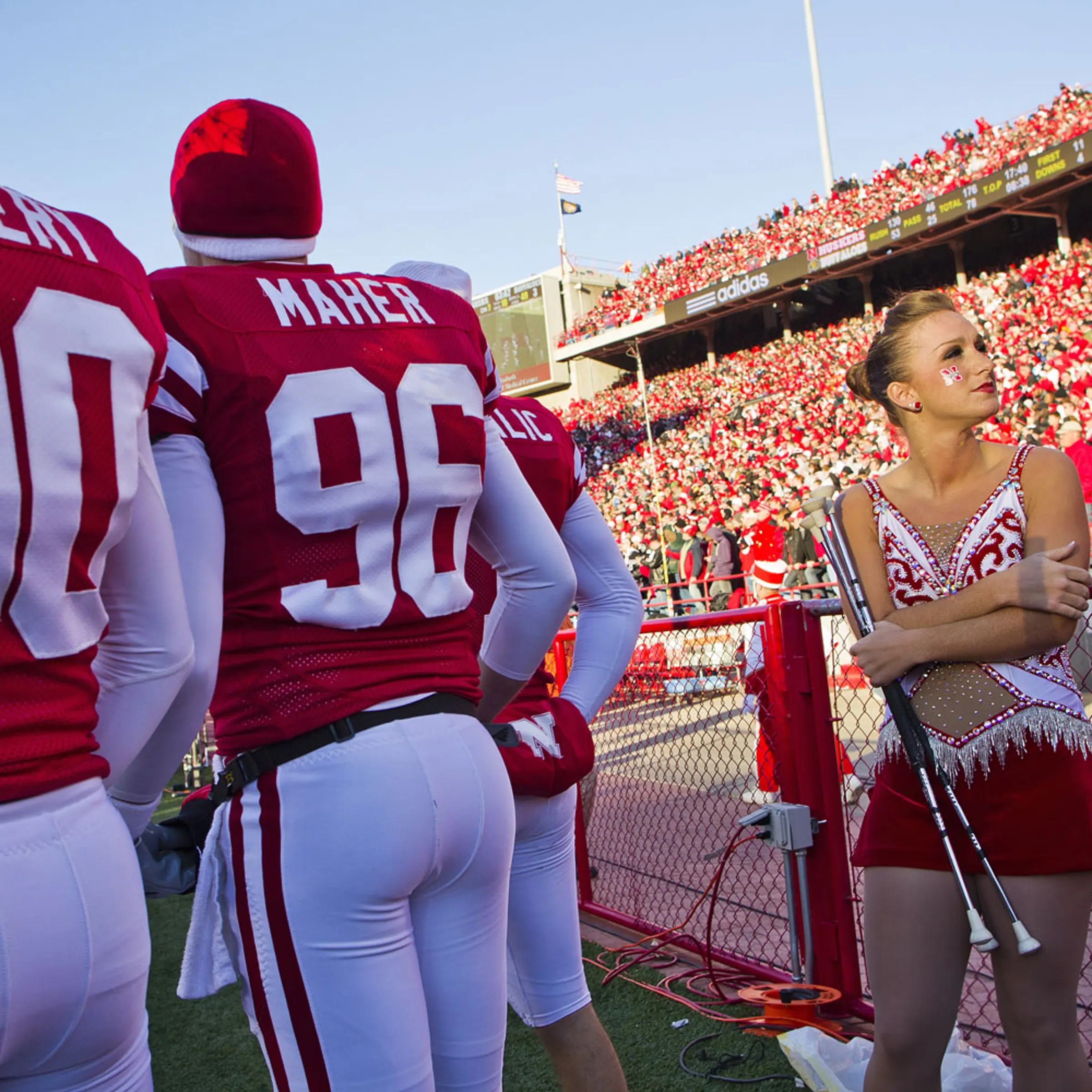 Nebraskaʼs baton twirler Rachel Foehlinger seeks warmth from a heater on the sidelines next to kickers Alex Henery and Brett Maher during a November 2010 game against Colorado.