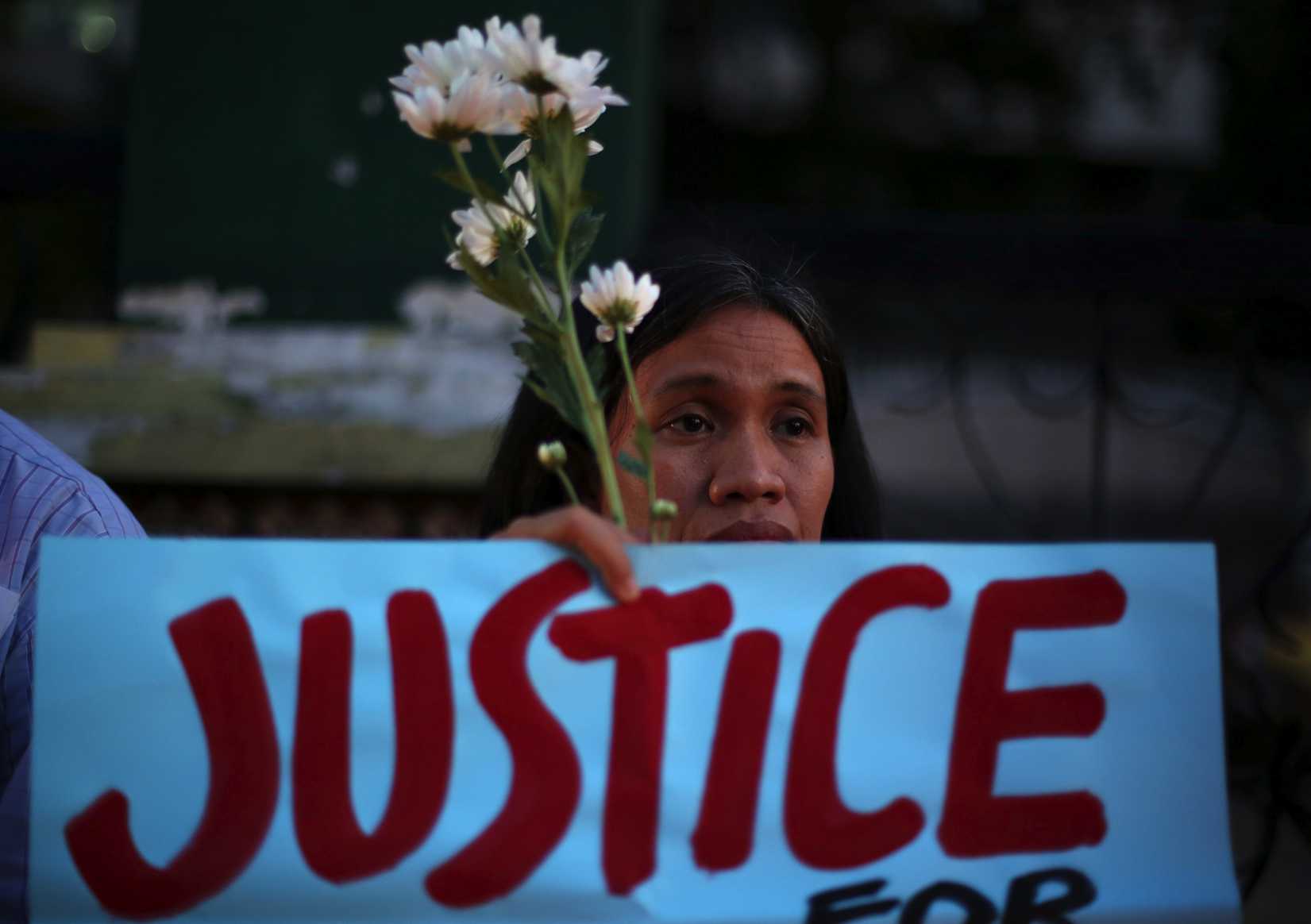 A Filipino activist holds flowers and a slogan during prayers in suburban Quezon city, Philippines on Thursday Oct. 23, 2014, to call for justice for the killing of Filipino transgender Jeffrey "Jennifer" Laude.