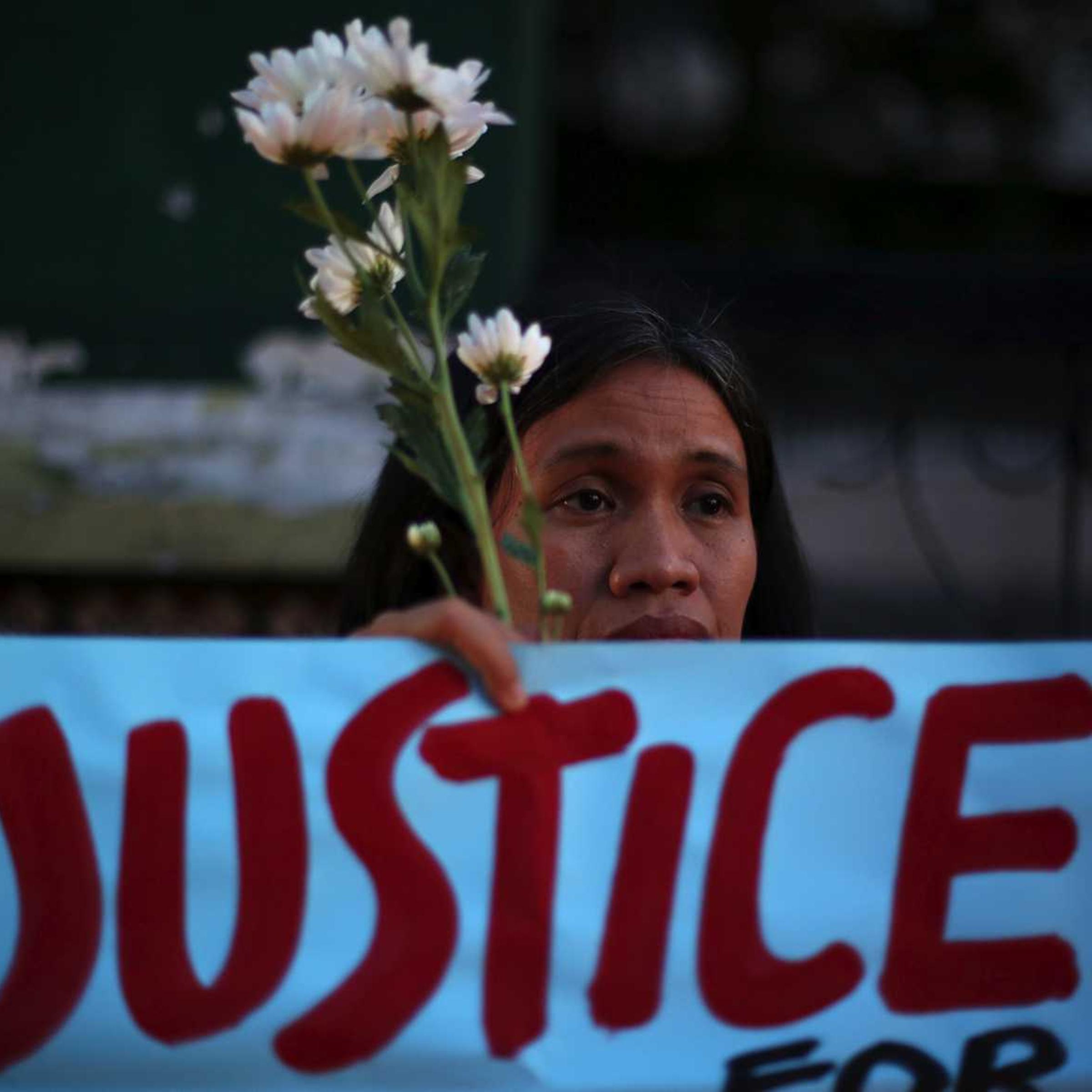 A Filipino activist holds flowers and a slogan during prayers in suburban Quezon city, Philippines on Thursday Oct. 23, 2014, to call for justice for the killing of Filipino transgender Jeffrey "Jennifer" Laude.
