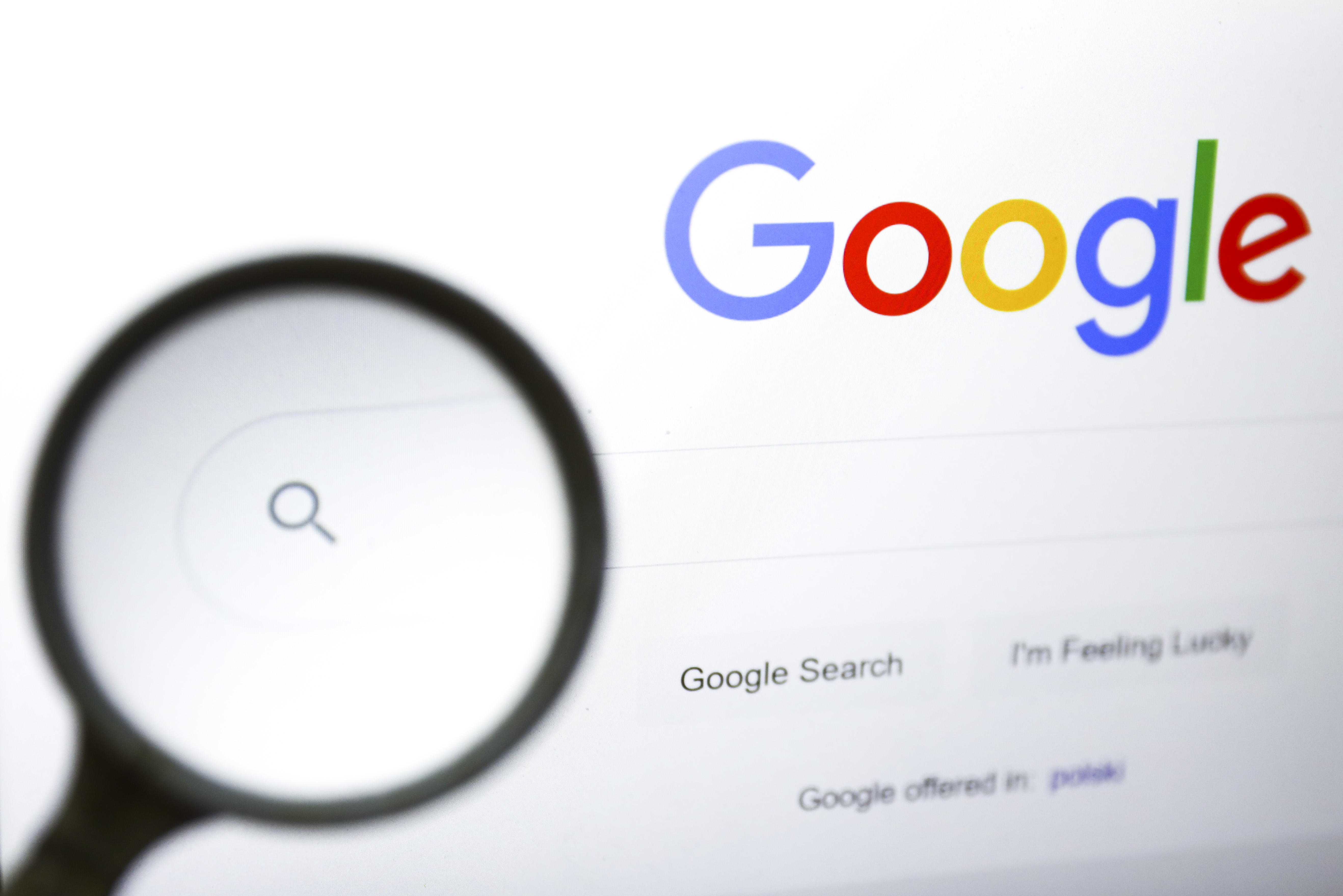 A magnifying glass is photographed with Google's logo displayed on a laptop screen.