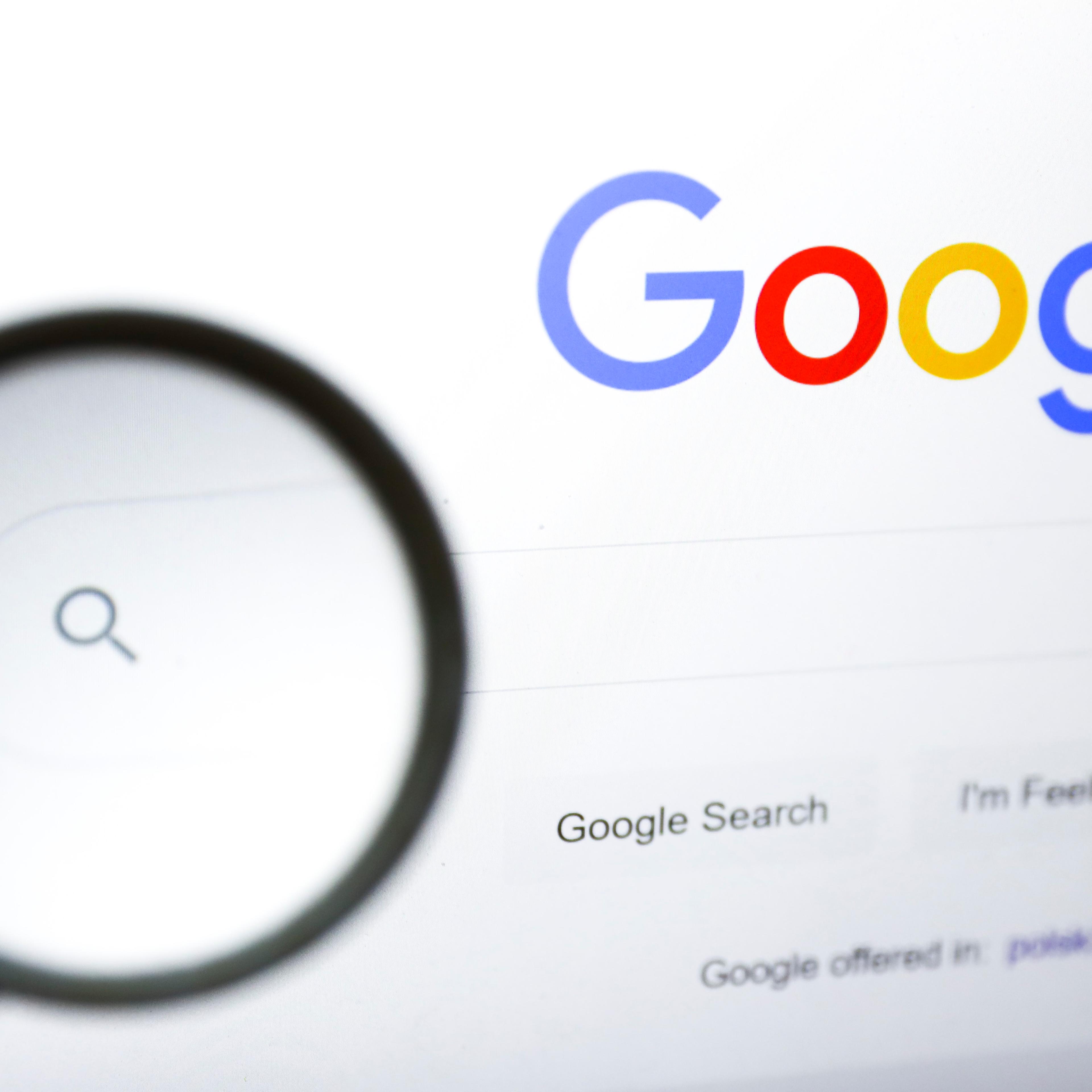 A magnifying glass is photographed with Google's logo displayed on a laptop screen.