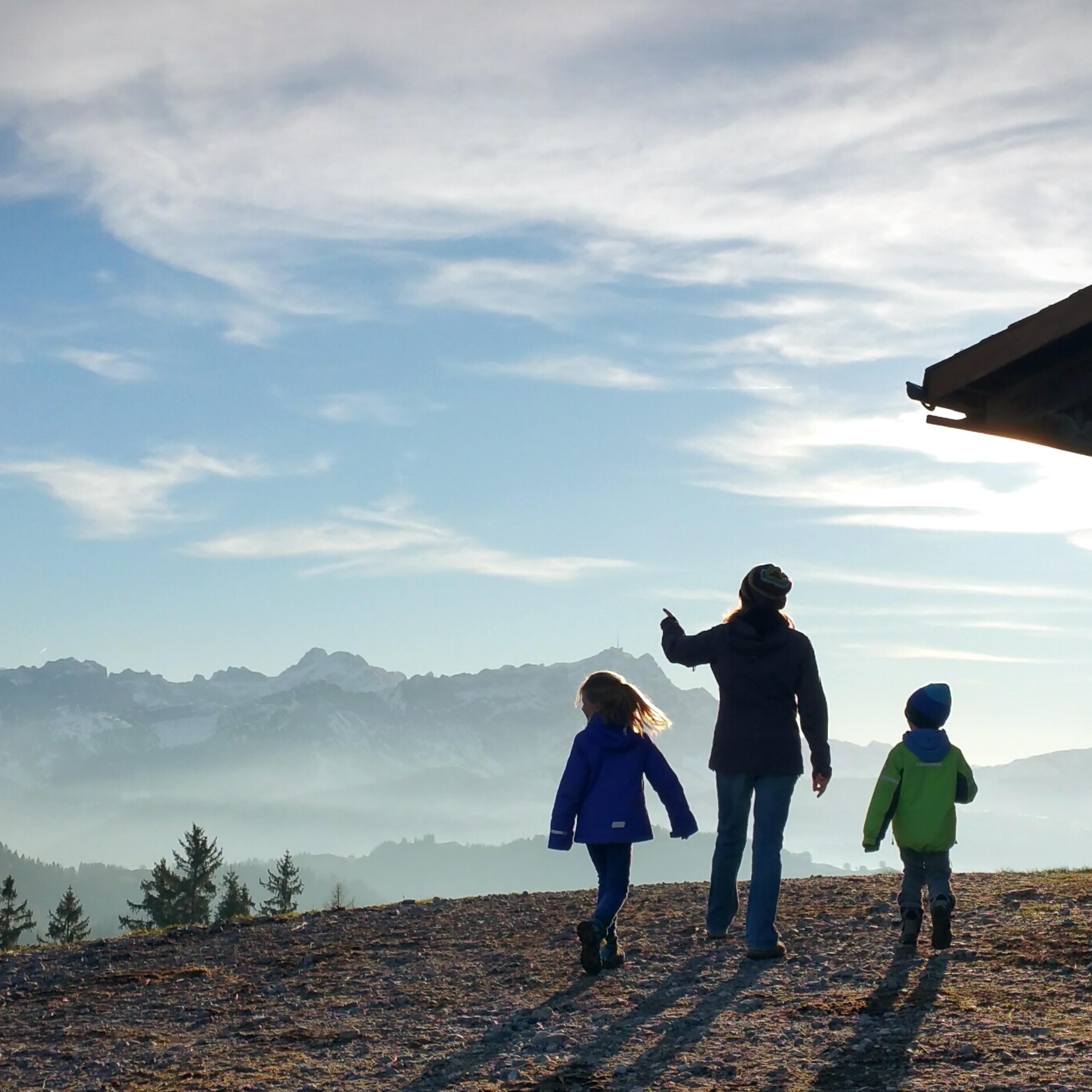 Rear View Of Mother And Children Standing On Hill Against Sky During Foggy Weather