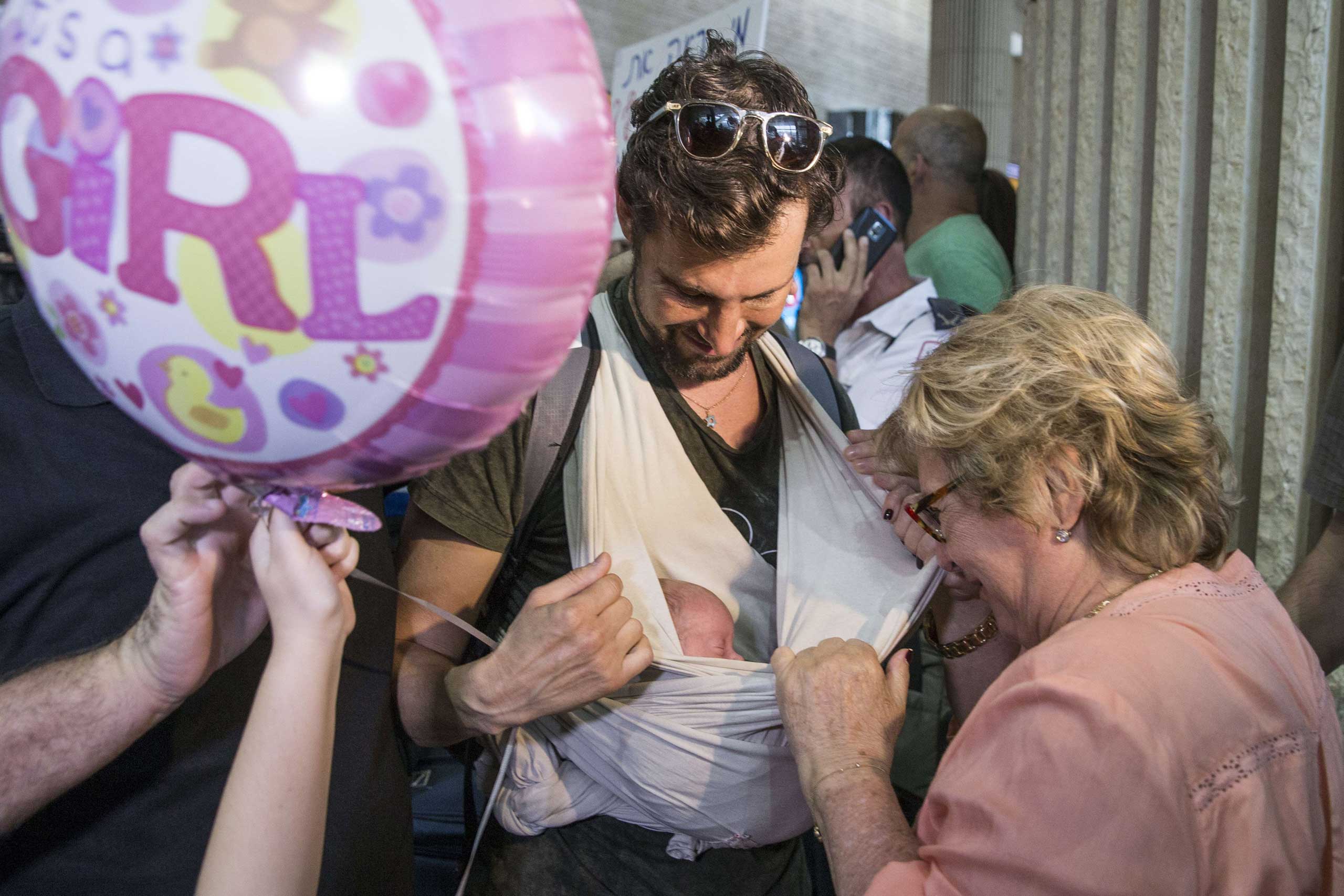 An Israeli gay man carries his baby born to a surrogate mother in Nepal as he is cheered by relatives at Ben Gurion airport near Tel Aviv on April 28, 2015, following his repatriation from the quake-hit Himalayan nation.