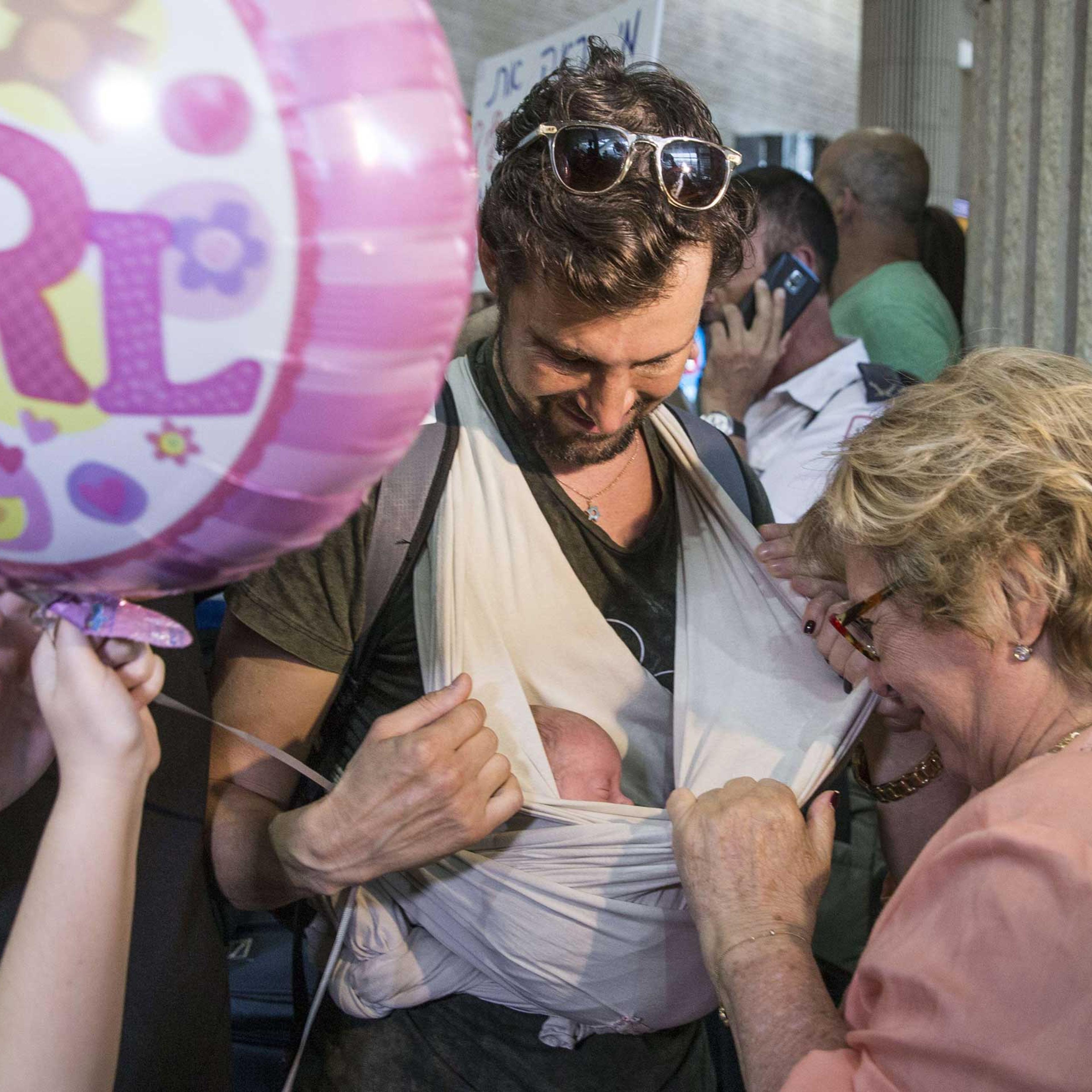 An Israeli gay man carries his baby born to a surrogate mother in Nepal as he is cheered by relatives at Ben Gurion airport near Tel Aviv on April 28, 2015, following his repatriation from the quake-hit Himalayan nation.