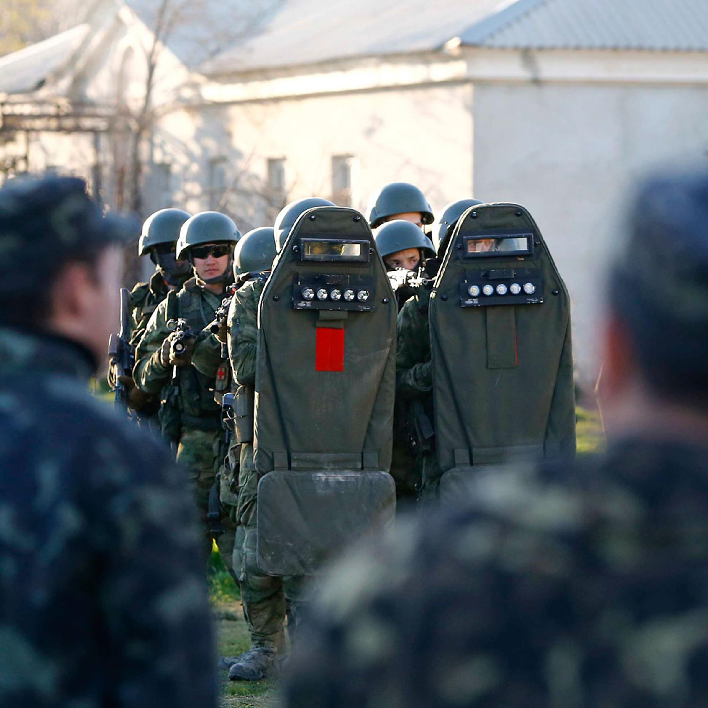 Armed men, believed to be Russian servicemen, stand guard, with Ukrainian servicemen seen in the foreground, at a military airbase, in the Crimean town of Belbek near Sevastopol
