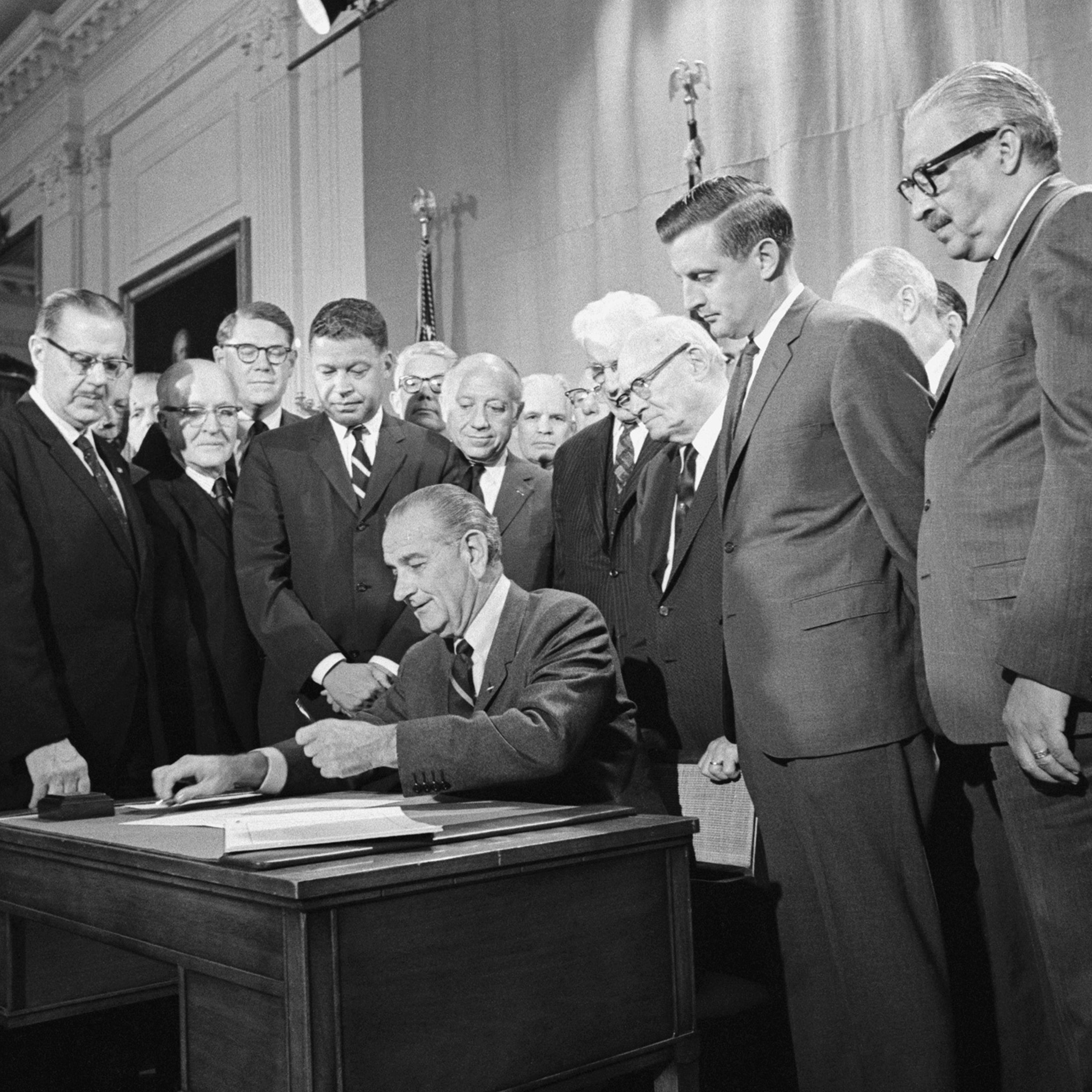 The Fair Housing Act's co-sponsors, Democratic Senator from Minnesota Walter Mondale (third from right) and Republican Senator from Massachusetts Edward Brooke (fourth from the left in the striped tie), watch President Lyndon B. Johnson sign the civil rights bill into law on April 11, 1968.