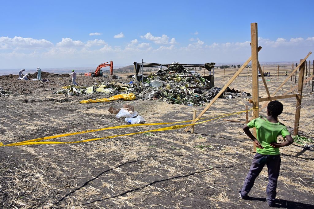 A boy looks as forensic investigators comb the ground for DNA evidence near a pile of twisted airplane debris at the crash site of an Ethiopian airways operated Boeing 737 MAX aircraft on March 16, 2019 at Hama Quntushele village near Bishoftu in Oromia 