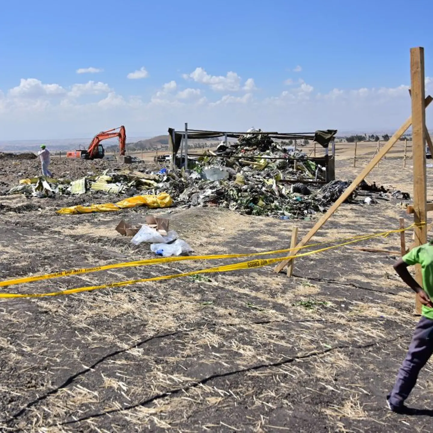 A boy looks as forensic investigators comb the ground for DNA evidence near a pile of twisted airplane debris at the crash site of an Ethiopian airways operated Boeing 737 MAX aircraft on March 16, 2019 at Hama Quntushele village near Bishoftu in Oromia