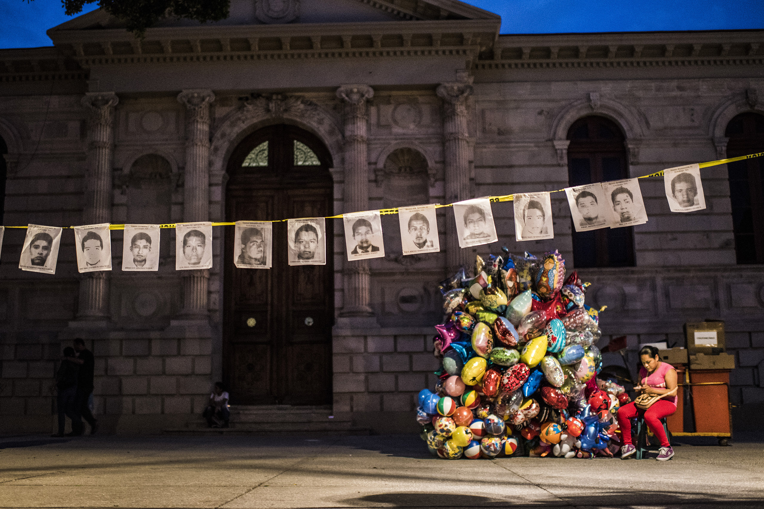 CHINPALCINGO, MEXICO - 31 OCTOBER 2014:Holding portraits of the missing students in Chinpalcingo Zocalo (Main Square) while a woman sell ballons for the Dia de los Muertos. Chilpancingo de los Bravo is the capital of Guerrero State and is located just 14
