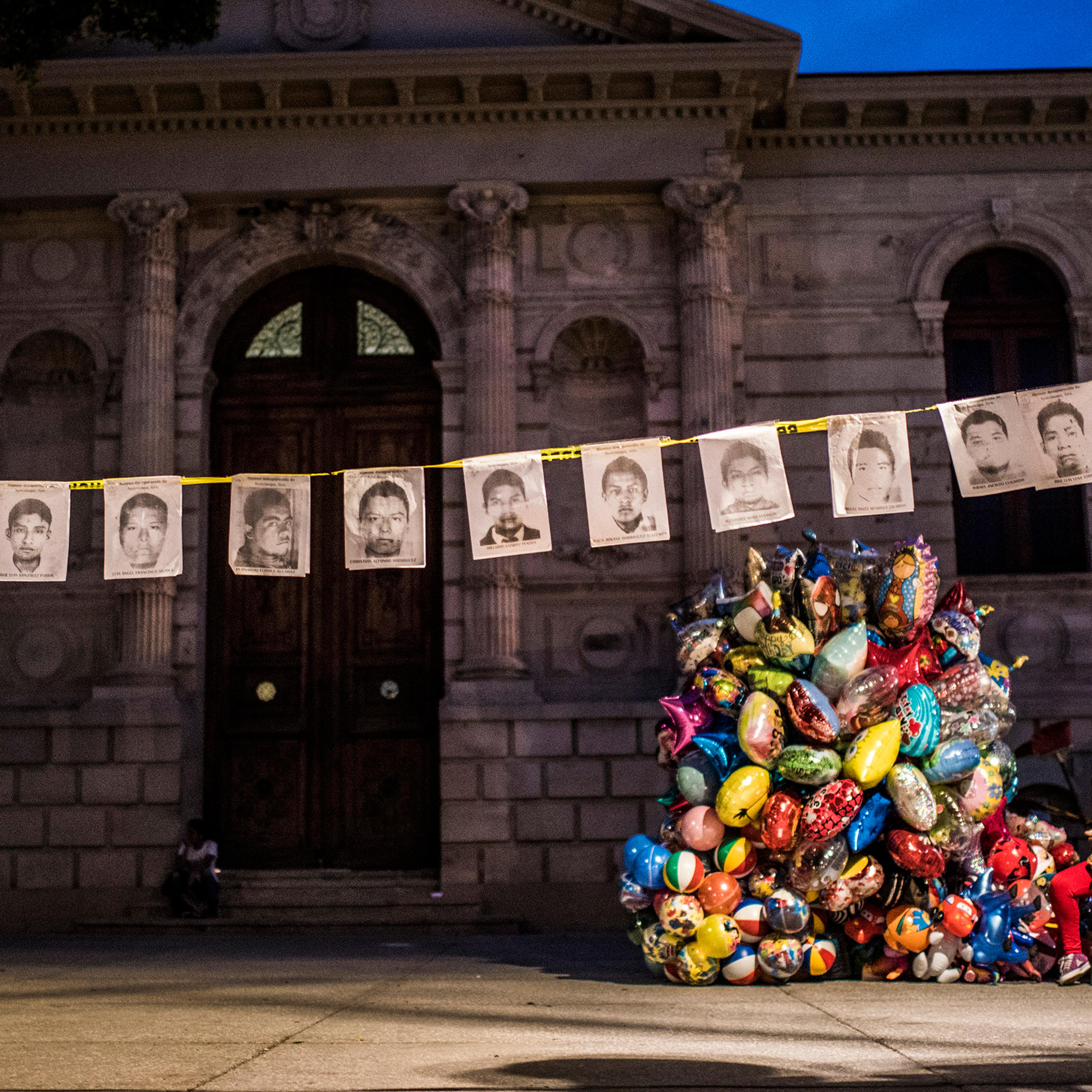 CHINPALCINGO, MEXICO - 31 OCTOBER 2014:Holding portraits of the missing students in Chinpalcingo Zocalo (Main Square) while a woman sell ballons for the Dia de los Muertos. Chilpancingo de los Bravo is the capital of Guerrero State and is located just 14