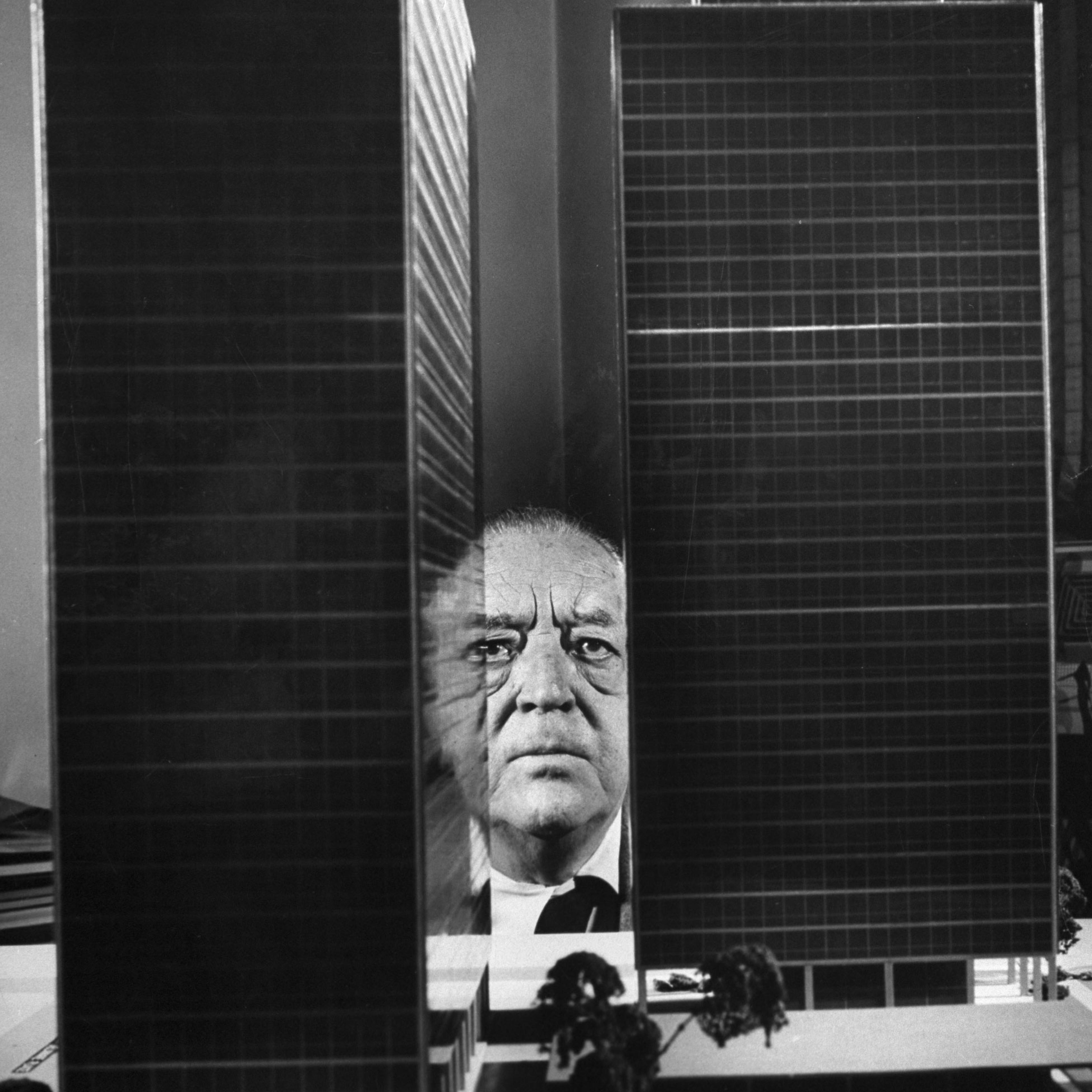 Architect Ludwig Mies van der Rohe peers between two large models of ultra-modern apartment buildings he designed for Chicago's Lake Shore Drive, 1956.