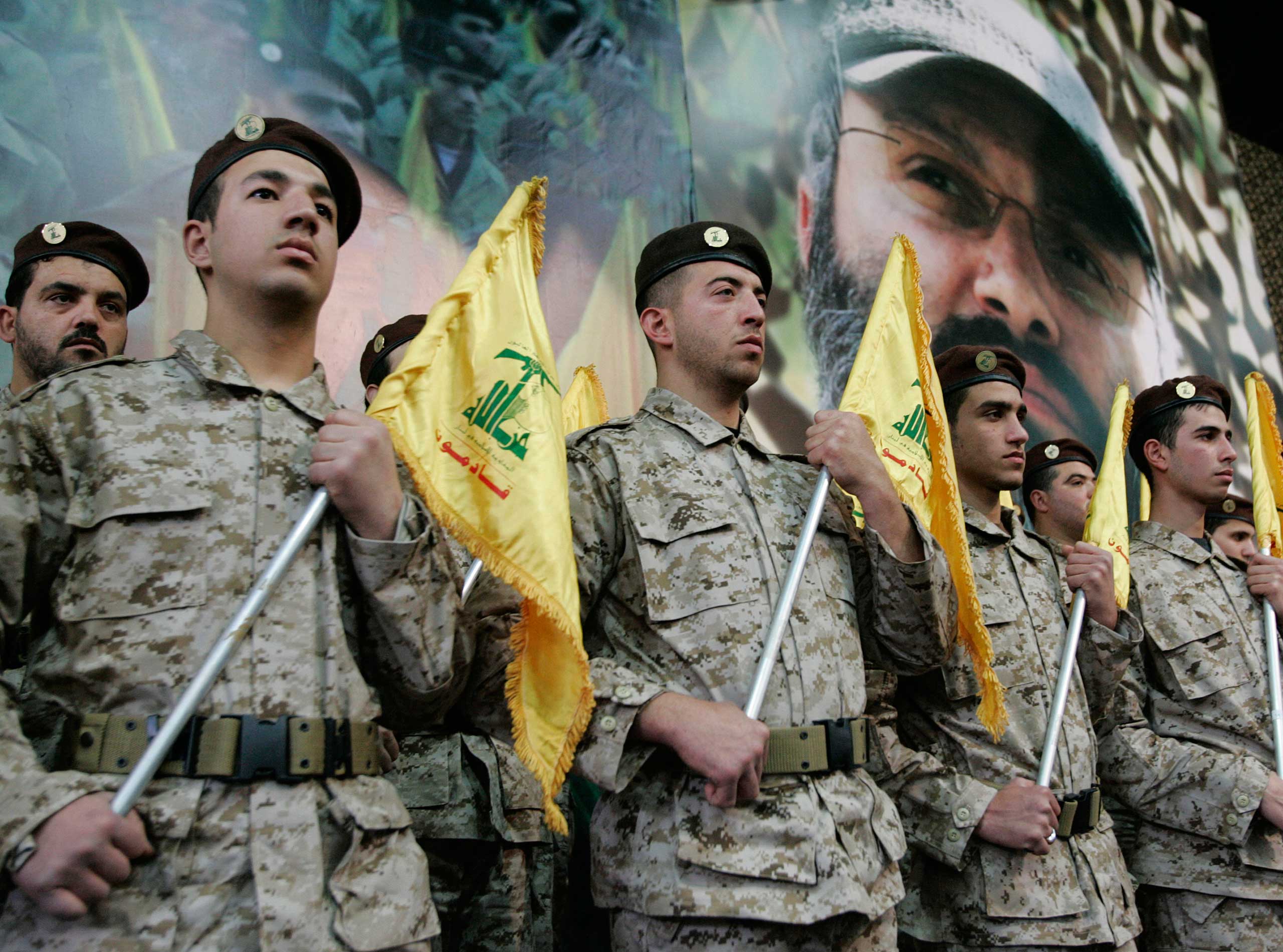 Hezbollah fighters hold their party flags and stand next to a portrait which shows their slain top commander Imad Mughniyeh, as they attend a rally to commemorate Mughniyeh and two other leaders, Abbas Musawi and Ragheb Harb, in the Shiite suburb of Beir