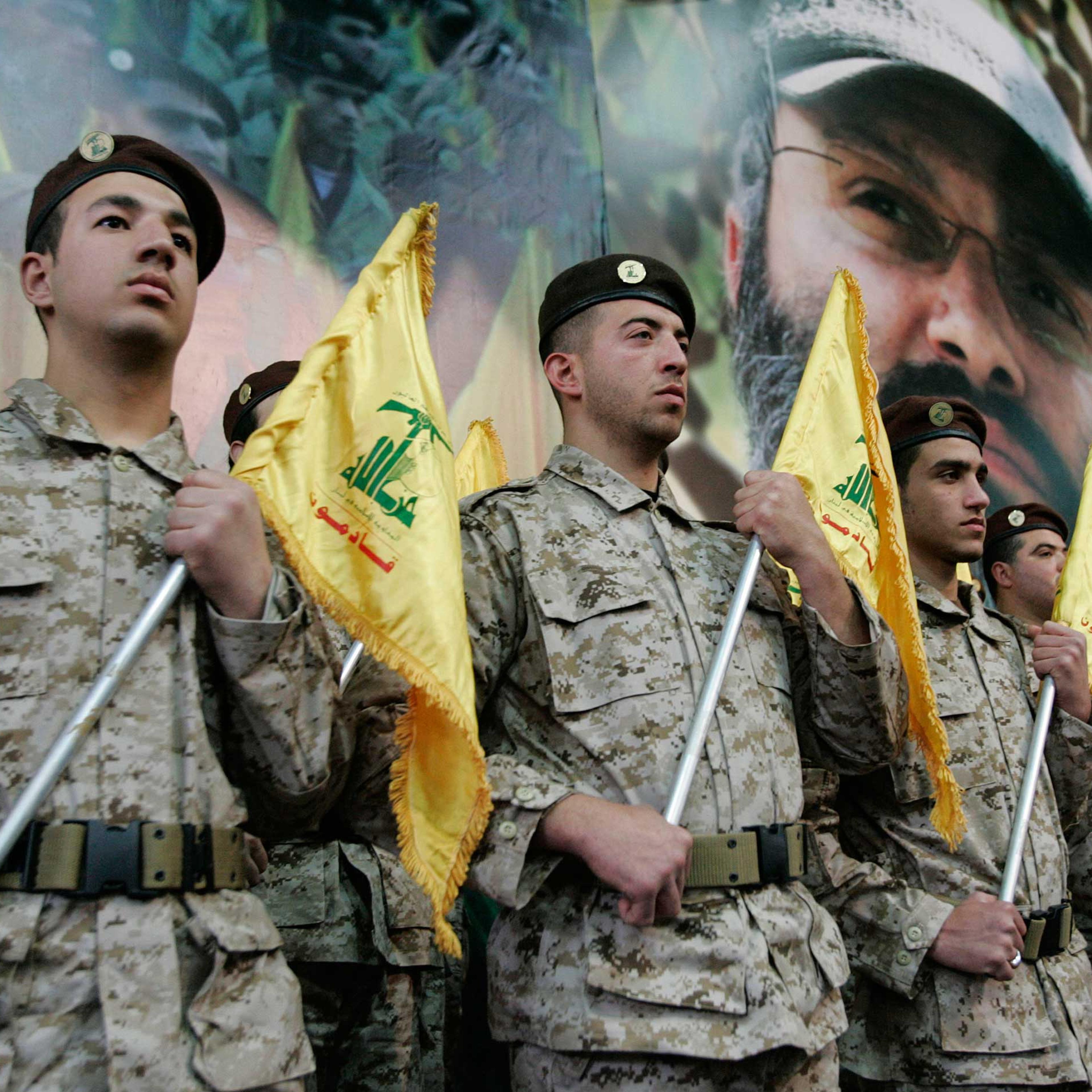 Hezbollah fighters hold their party flags and stand next to a portrait which shows their slain top commander Imad Mughniyeh, as they attend a rally to commemorate Mughniyeh and two other leaders, Abbas Musawi and Ragheb Harb, in the Shiite suburb of Beir