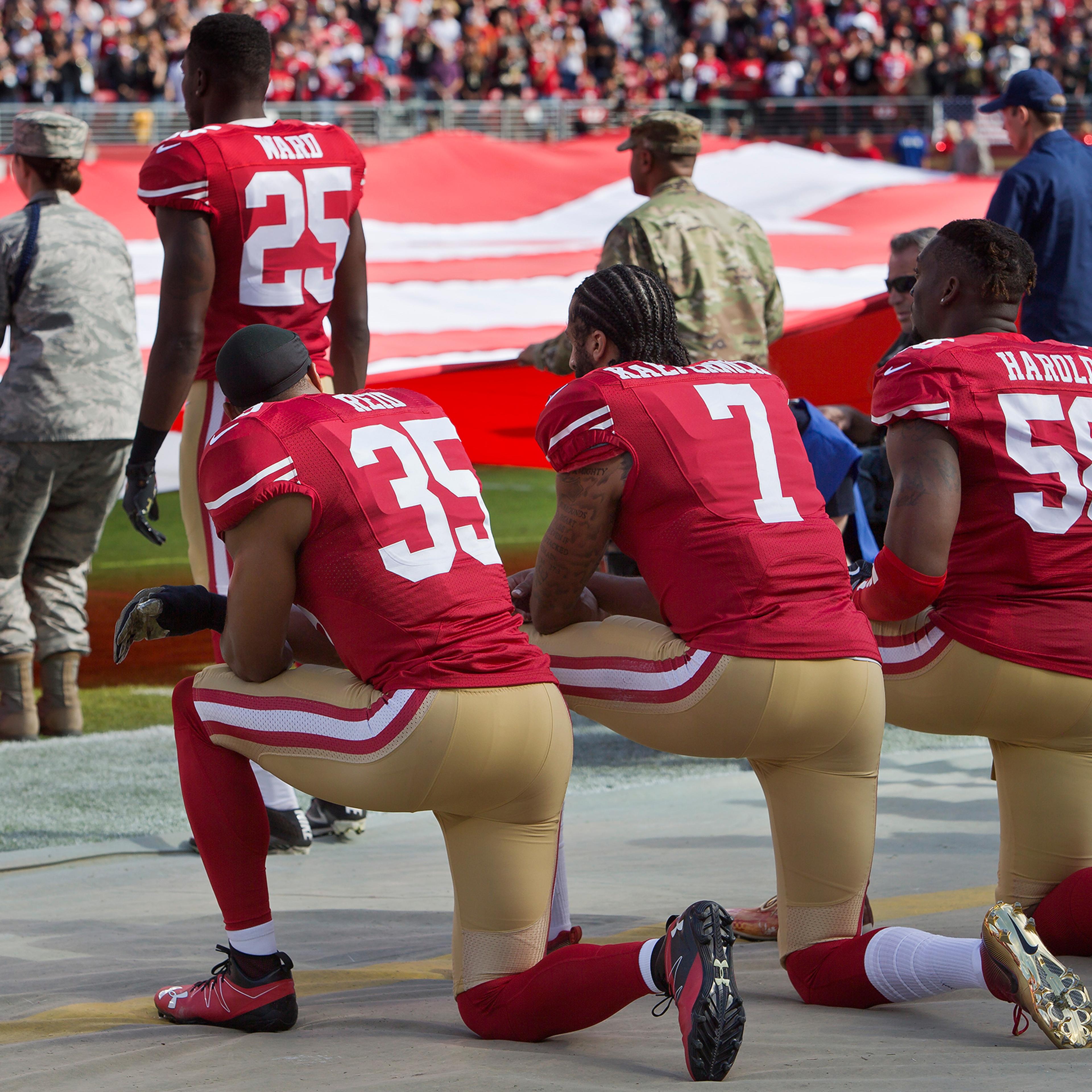 Quarterback Colin Kaepernick #7, safety Eric Reid #35, and linebacker Eli Harold #58 of the San Francisco 49ers kneel before a game against the New Orleans Saints with the U.S. flag unfurled in honor of the armed services on Nov. 6 2016 at Levi's Stadium