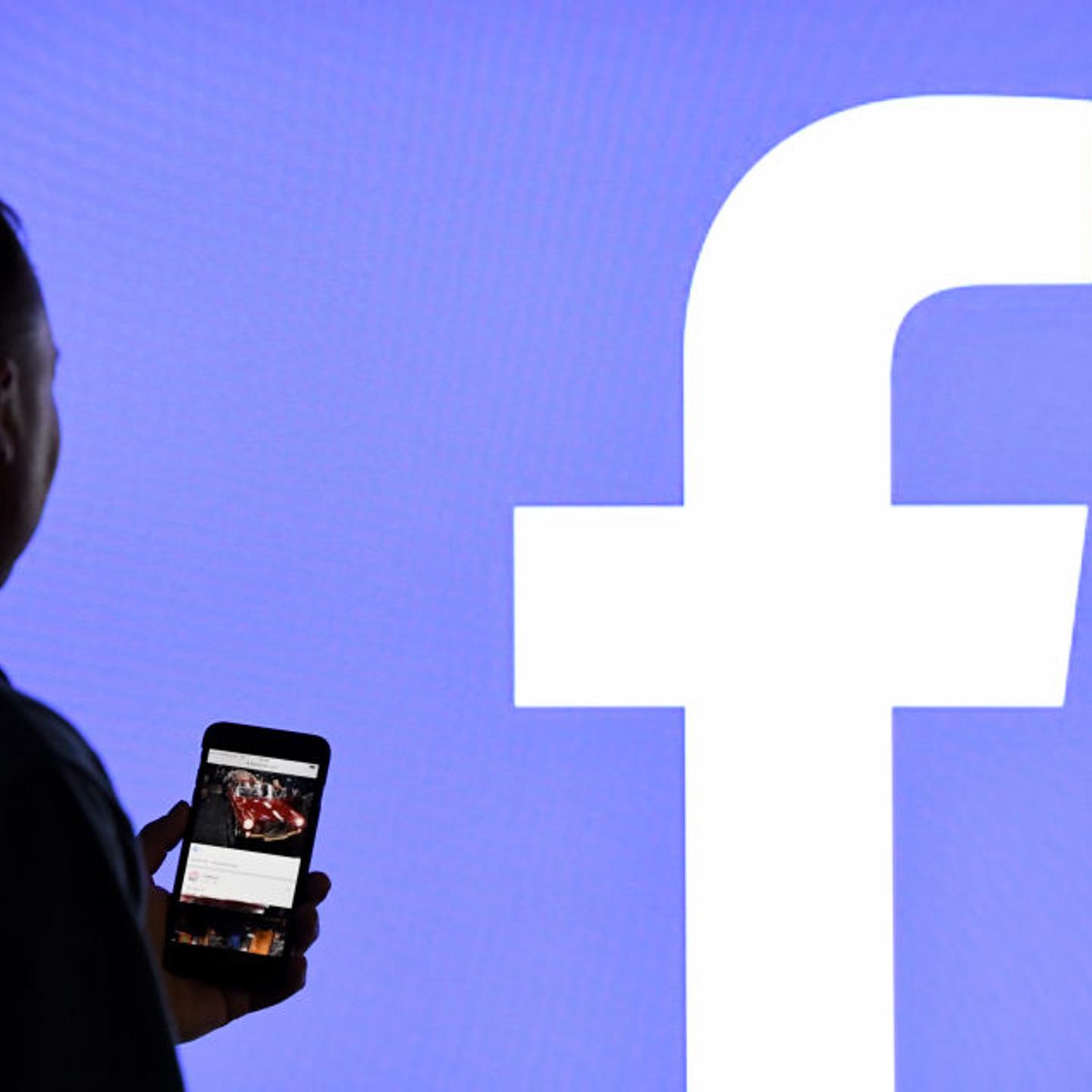 Man Stands in Front of Facebook Logo Screen