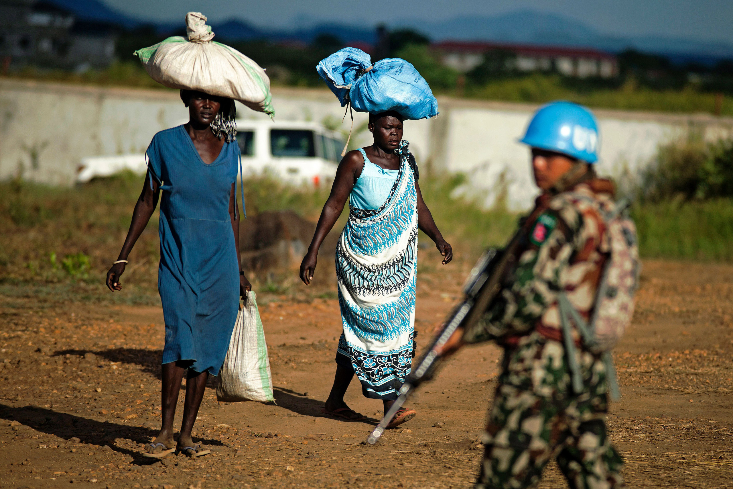 Displaced women carry goods as a Nepalese peacekeeper from the United Nations Mission in South Sudan (UNMISS) patrols outside the premises of the UN Protection of Civilians (PoC) site in Juba on October 4, 2016. According to the UN, due to the increase o
