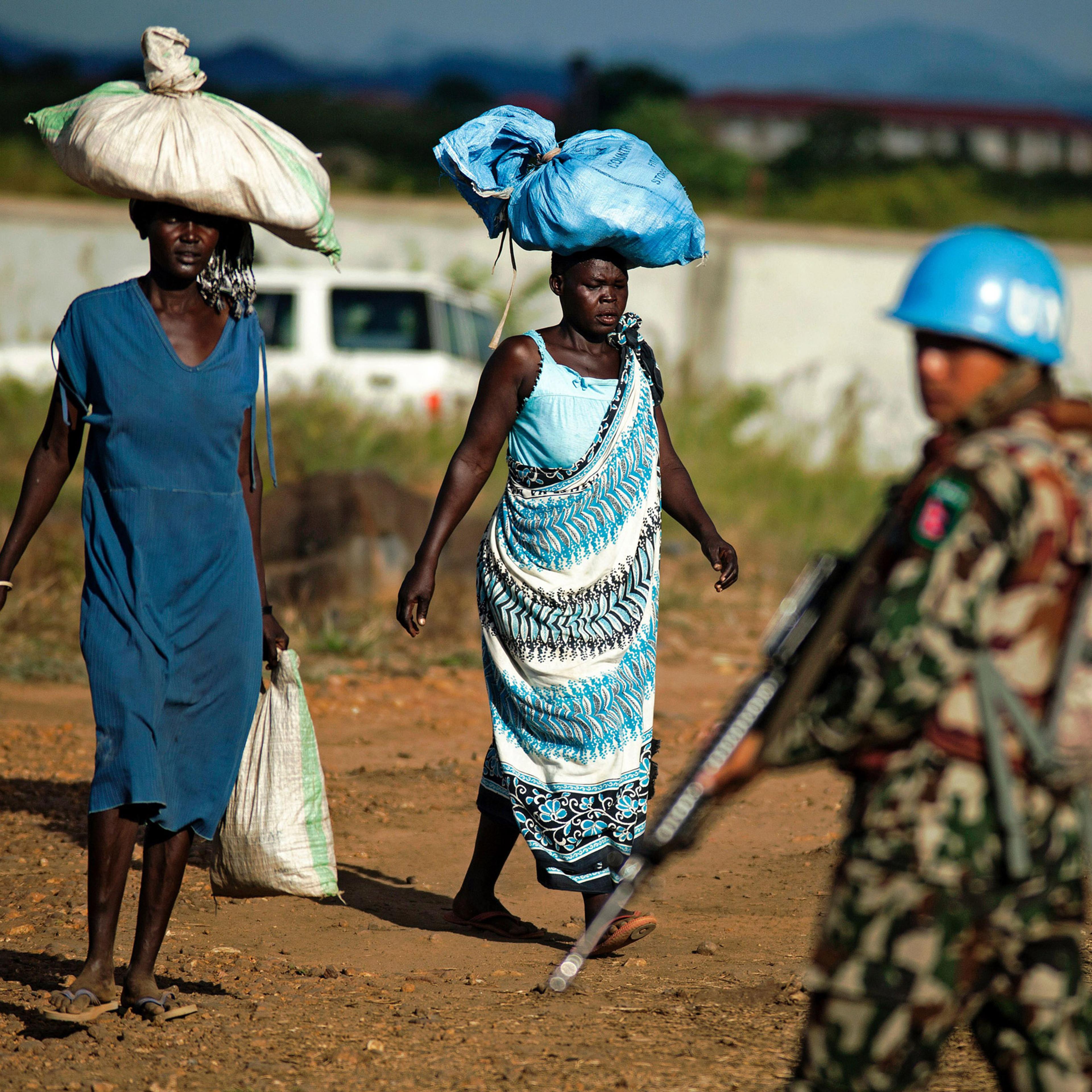 Displaced women carry goods as a Nepalese peacekeeper from the United Nations Mission in South Sudan (UNMISS) patrols outside the premises of the UN Protection of Civilians (PoC) site in Juba on October 4, 2016. According to the UN, due to the increase o