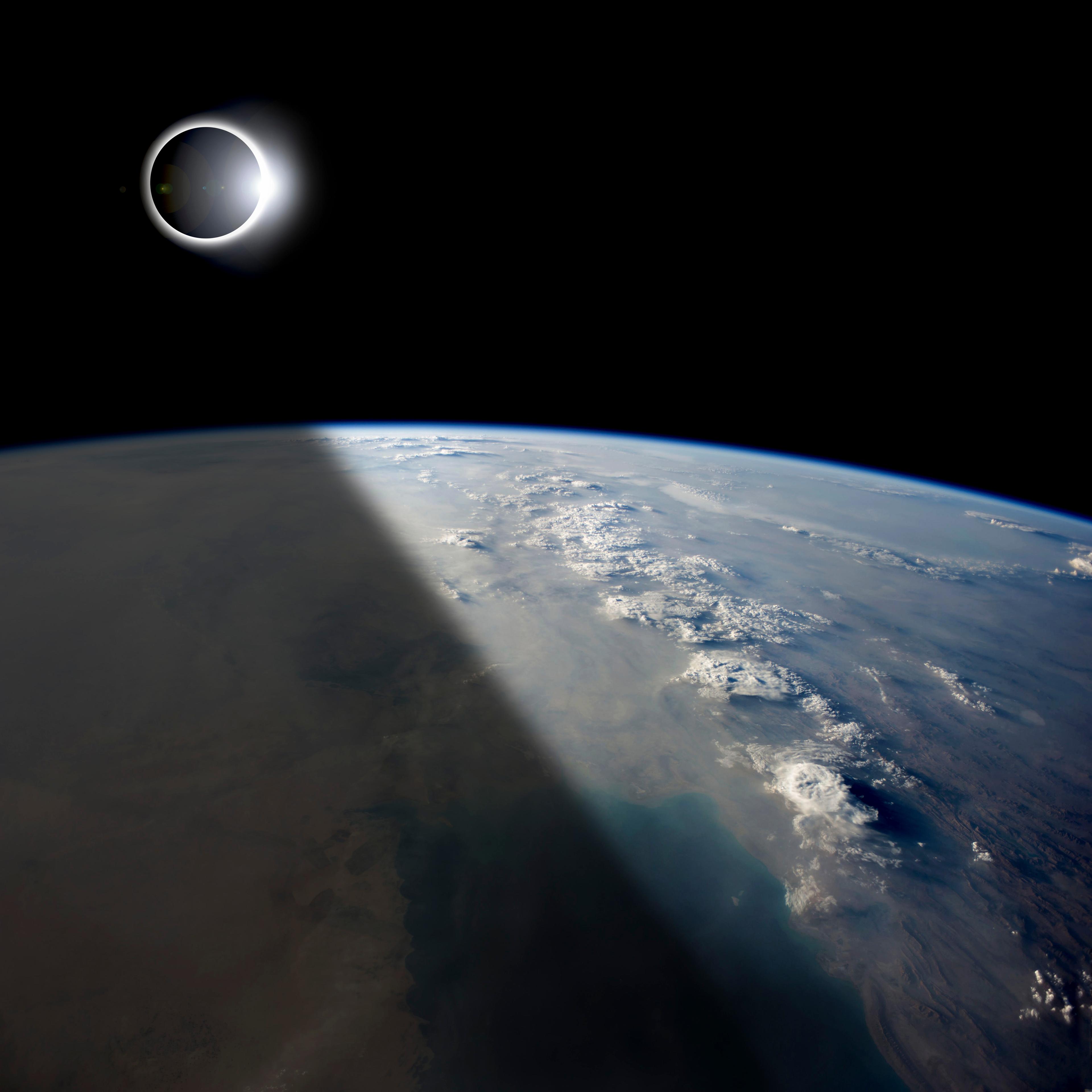 A solar eclipses partially shades the Earth below while the emerging sun lights the remainder of the planet.