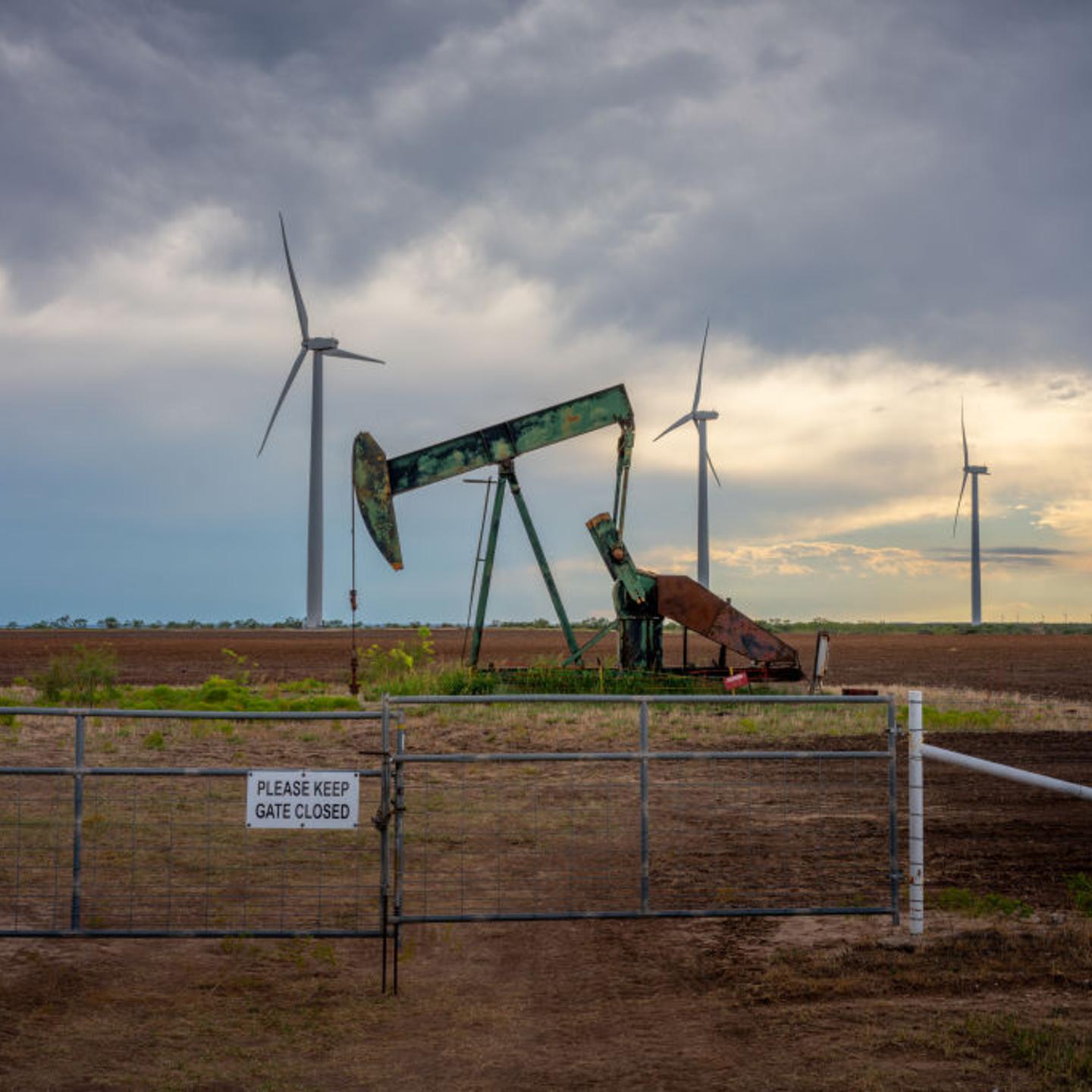 An oil pump jack with with wind turbines in the background
