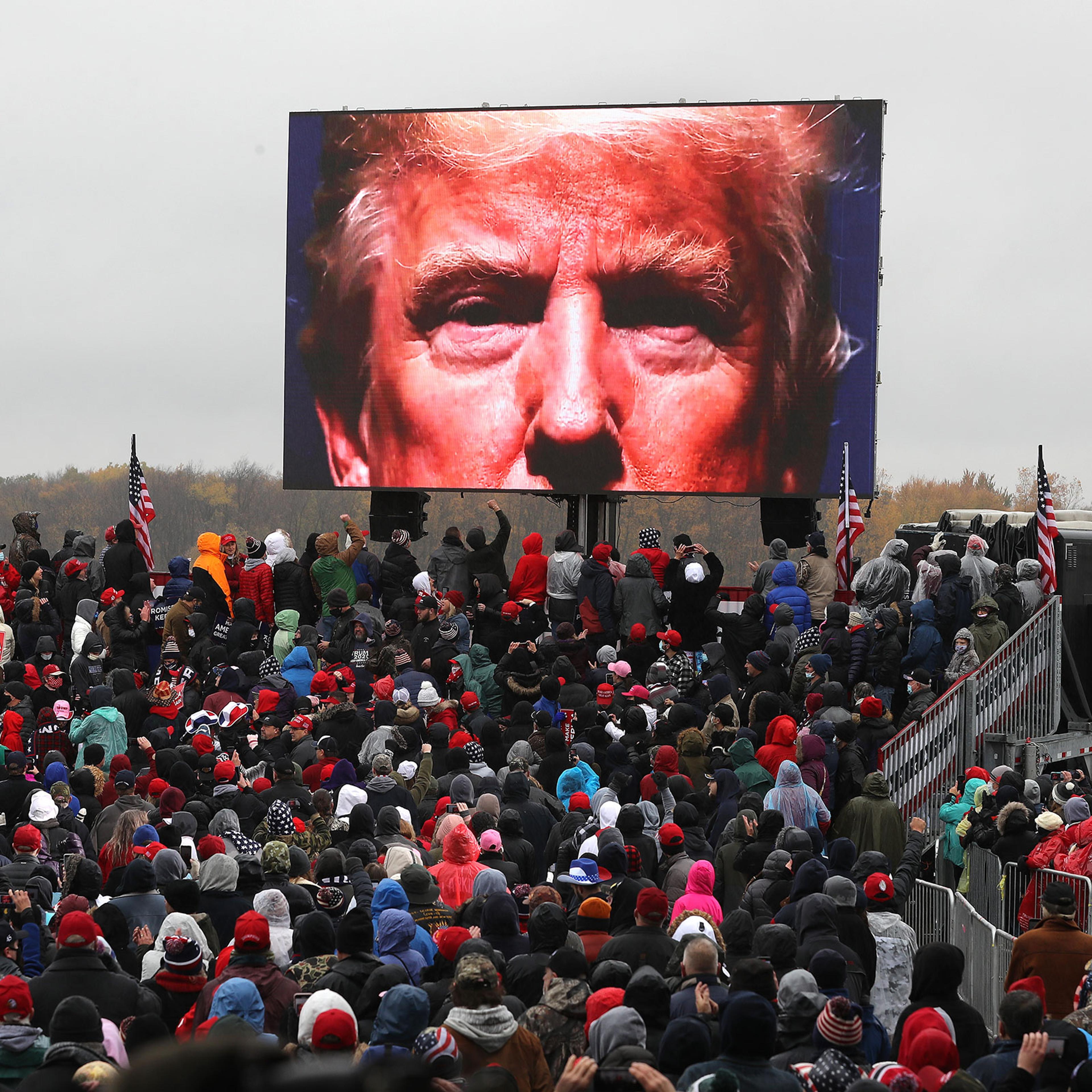 Supporters watch a video of President Donald Trump while waiting for his arrival at a campaign rally at Capital Region International Airport in Lansing, Mich. on Oct. 27, 2020.