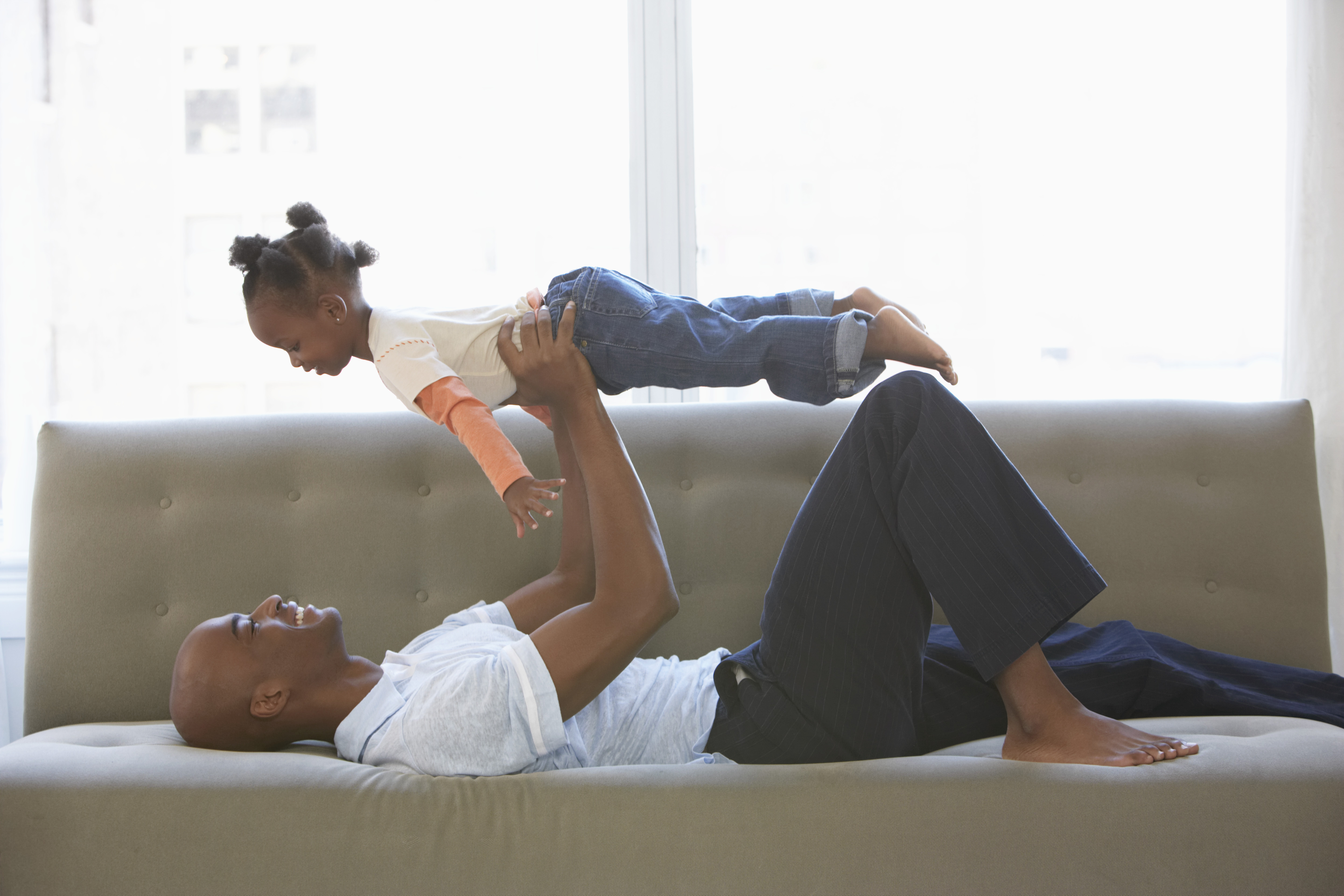 Father lying on sofa, holding daughter (2-4) up