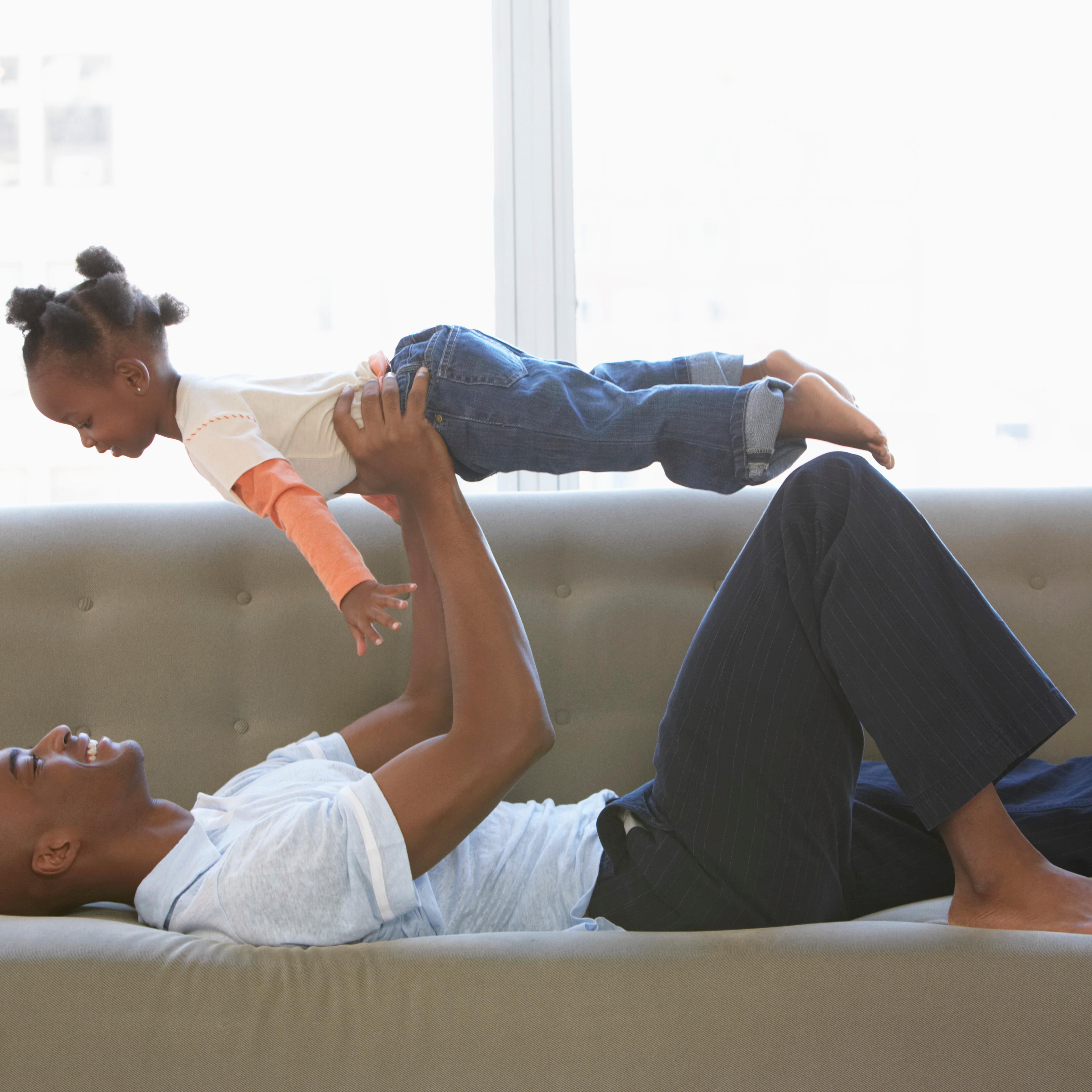 Father lying on sofa, holding daughter (2-4) up