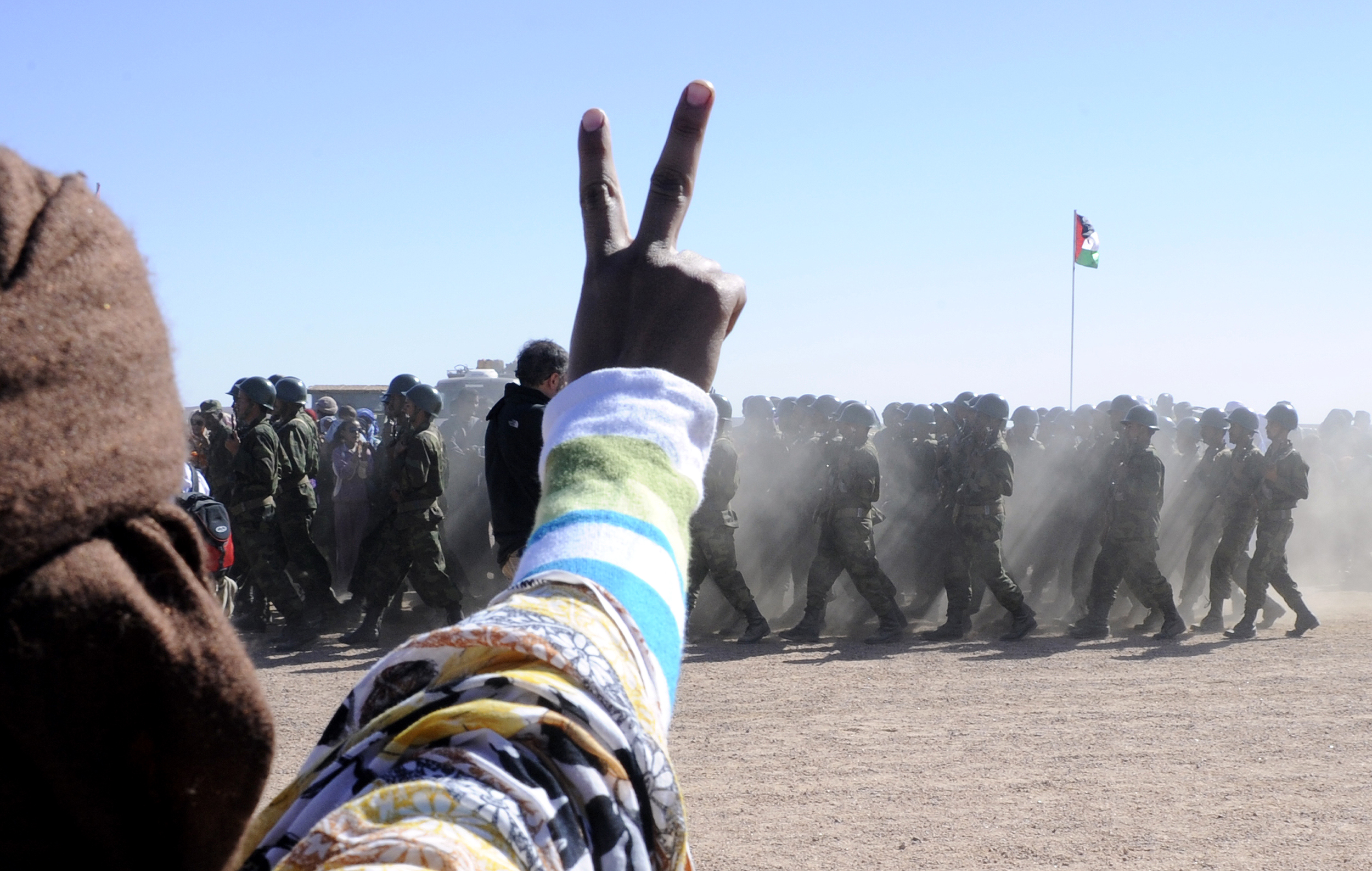 A man flashes a v-sign as soldiers from