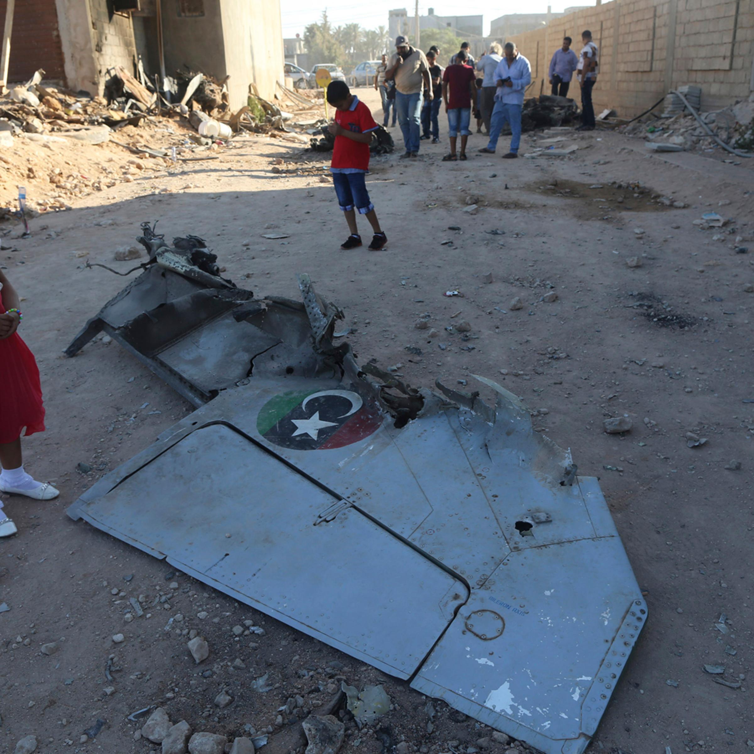 A girl stands next to the wreckage of a government MiG warplane which crashed during Tuesday's fighting, in Benghazi