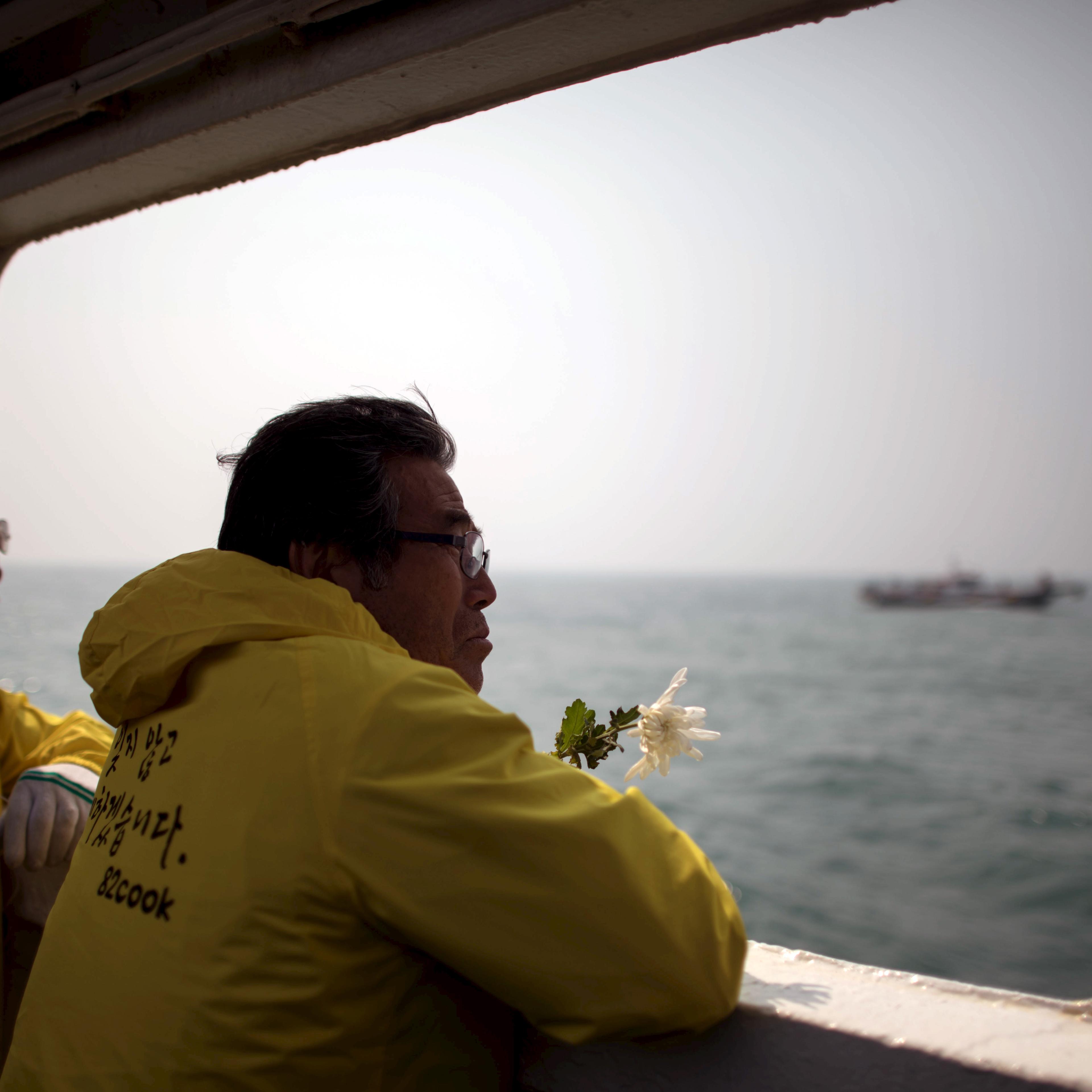 A relative of a victim of the Sewol ferry disaster holds a flower as he stands on the deck of a boat during a visit to the site of the sunken ferry, off the coast of South Korea's southern island of Jindo