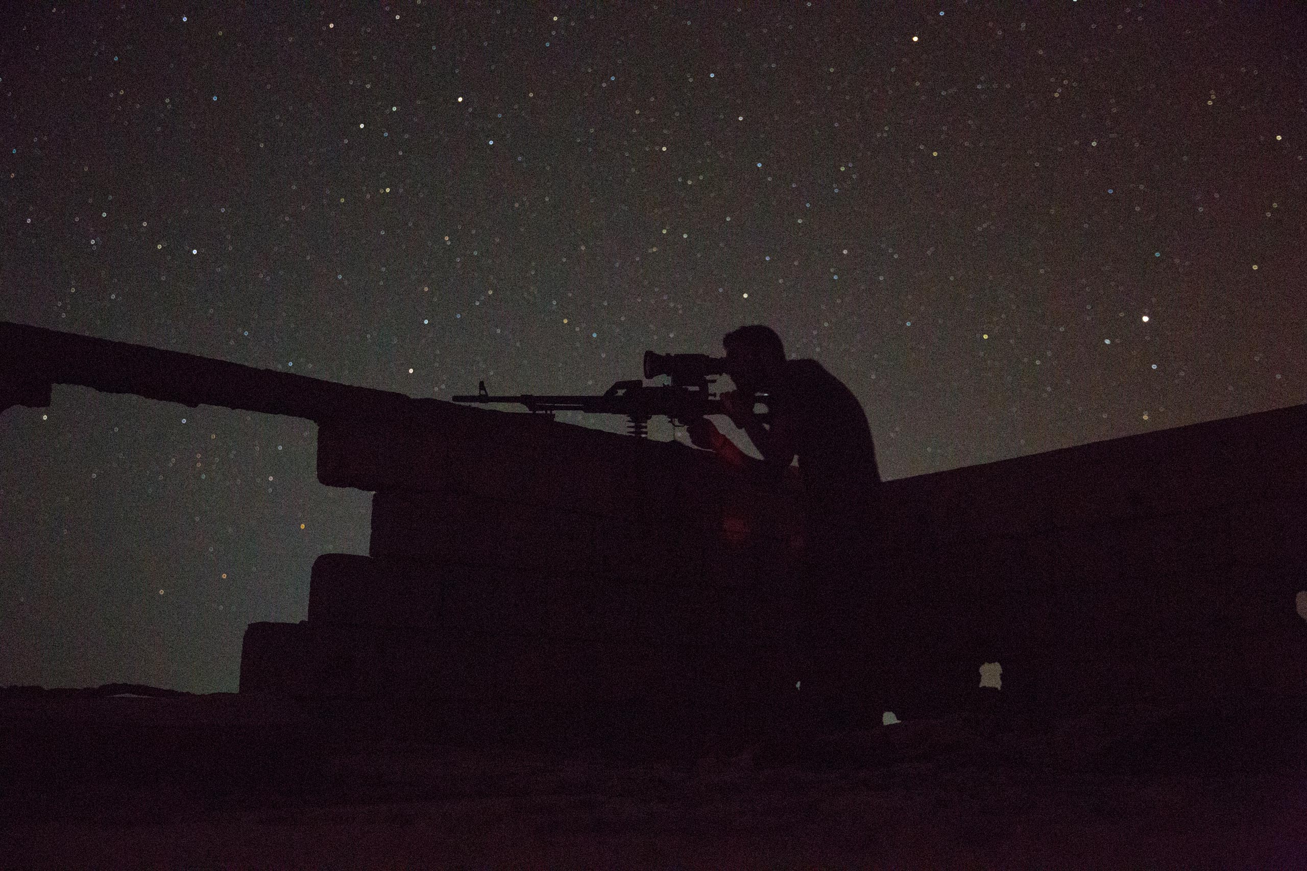 Jibril, a Christian fighter with the Syrian government's Directorate of Military Intelligence, surveys known ISIS positions using a night vision scope mounted on a Russian squad assault weapon, May 20, 2015.