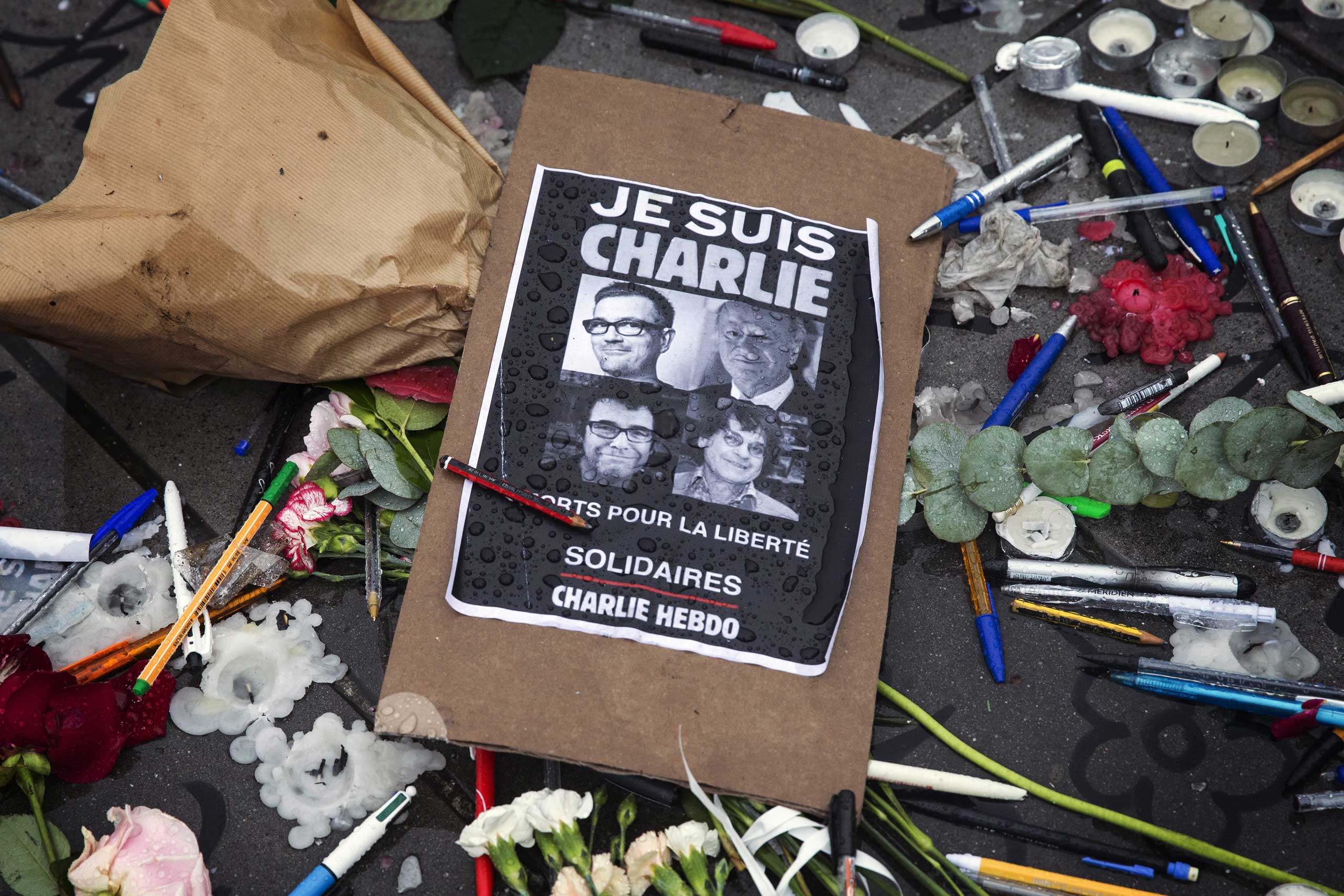 A poster reads 'Je suis Charlie' (I am Charlie) amid symbolic pens and pencils on Place de la Republique as people gather for a minute of silence commemorating those killed in a shooting at French satirical magazine 'Charlie Hebdo', in Paris, Jan. 8, 201