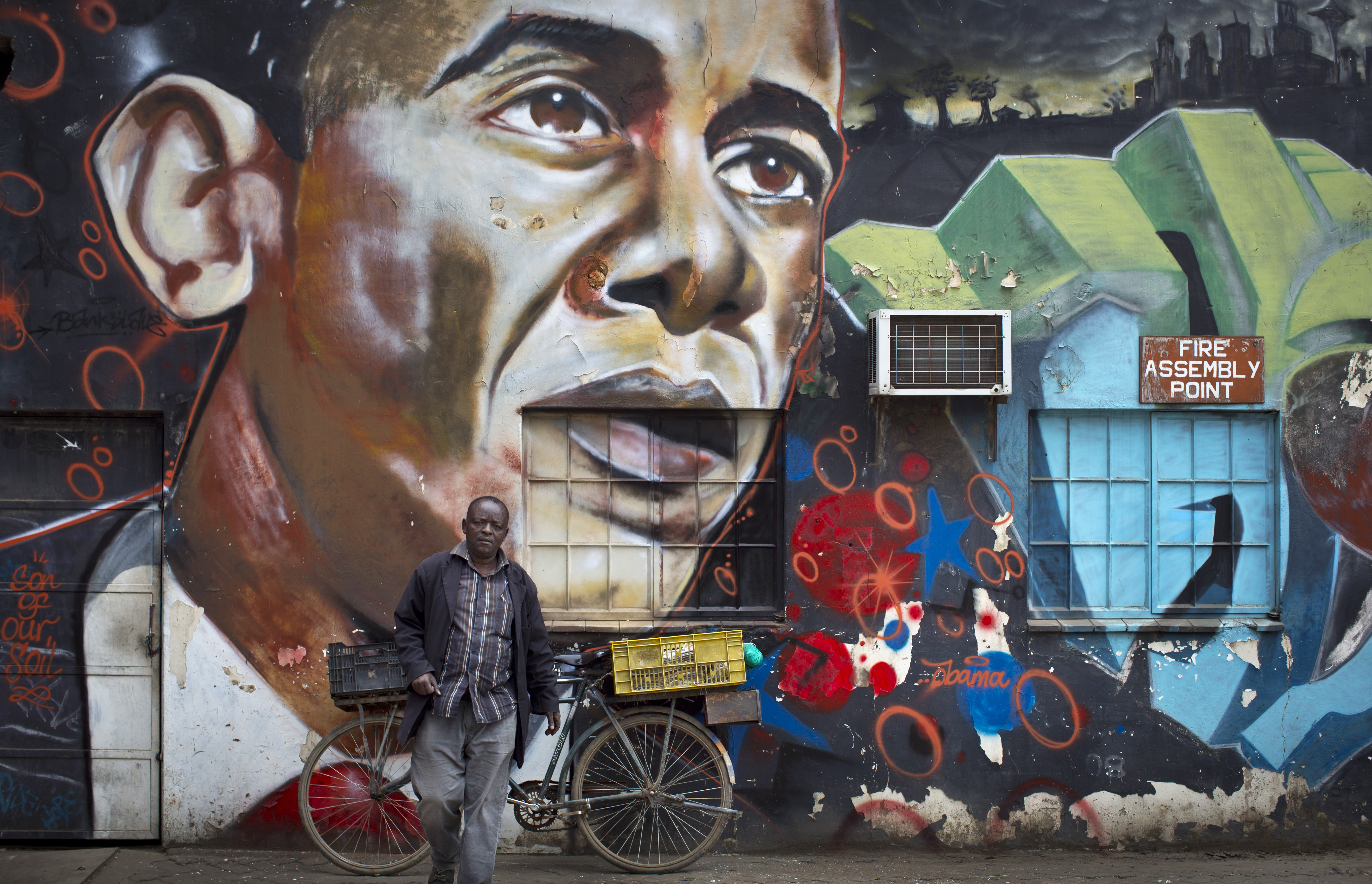 A man walks away after leaning his bicycle against a mural of President Barack Obama, created by the Kenyan graffiti artist Bankslave, at the GoDown Arts Centre in Nairobi on July 22, 2015.