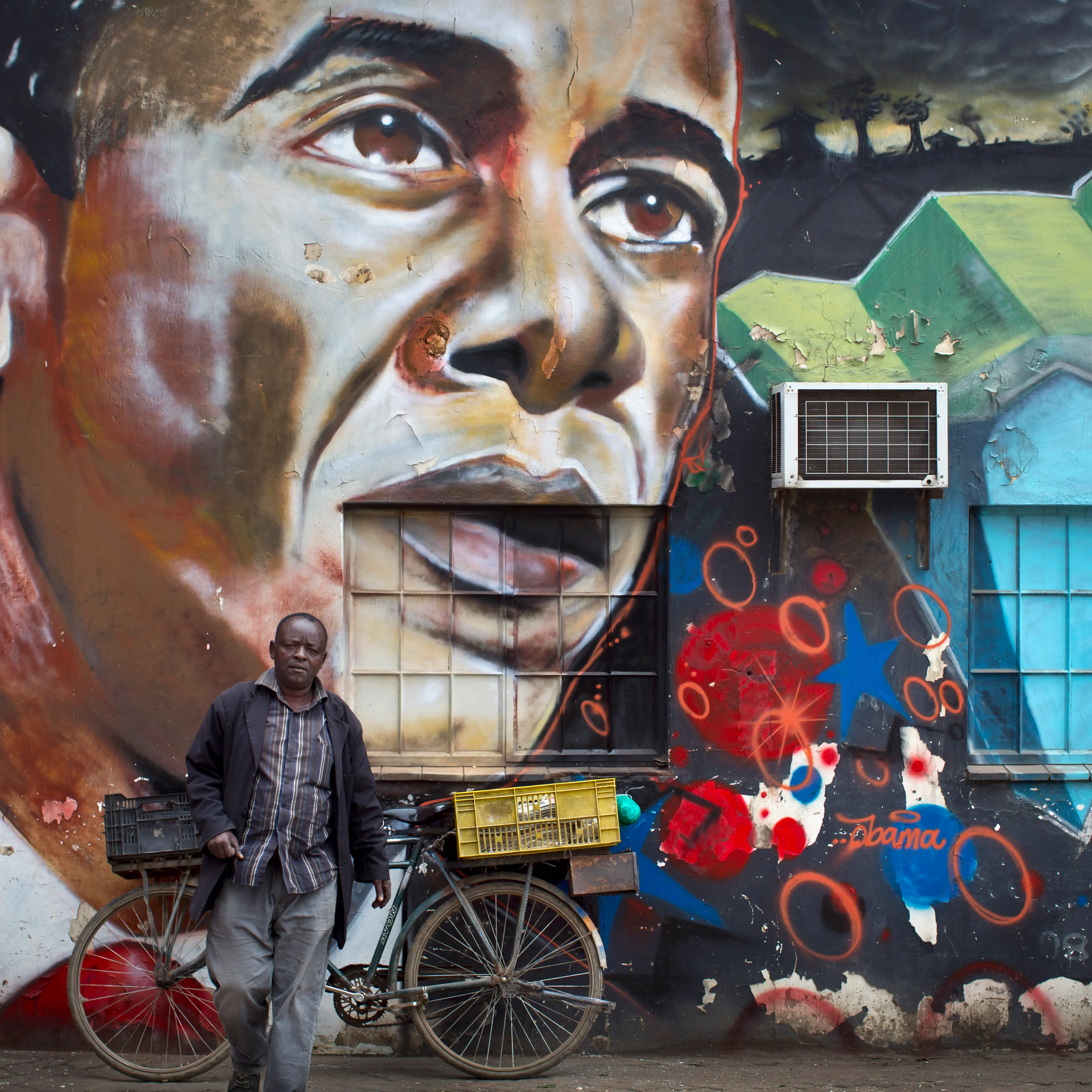 A man walks away after leaning his bicycle against a mural of President Barack Obama, created by the Kenyan graffiti artist Bankslave, at the GoDown Arts Centre in Nairobi on July 22, 2015.