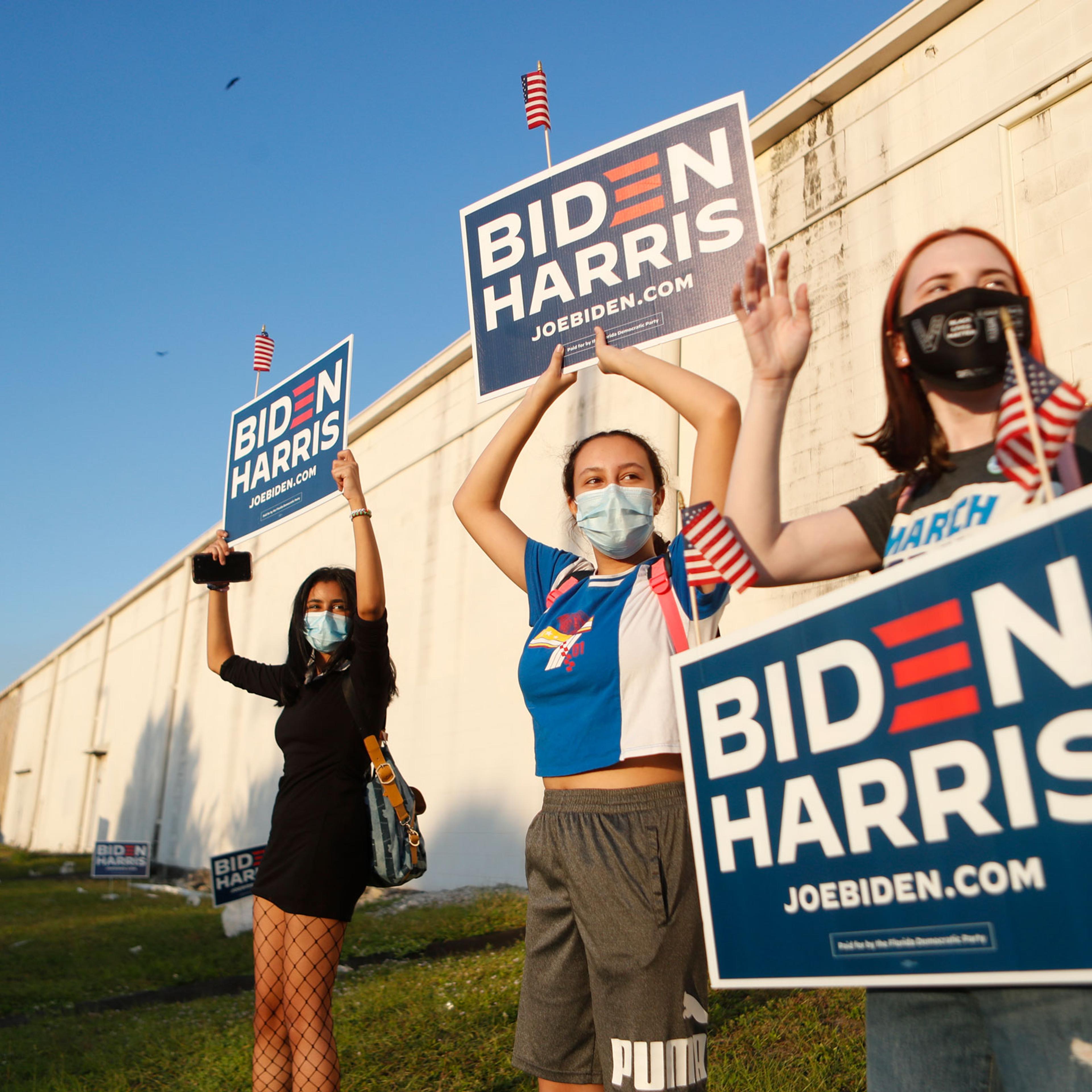 Three young women wave their Biden-Harris signs at the Town 'N Country Regional Public Library