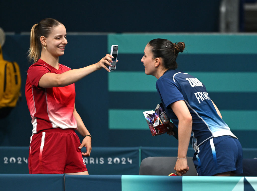 France's table tennis player Charlotte Lutz (left) shows her phone to France's table tennis player Audrey Zarif after their training session at South Arena in Paris on July 23, 2024.