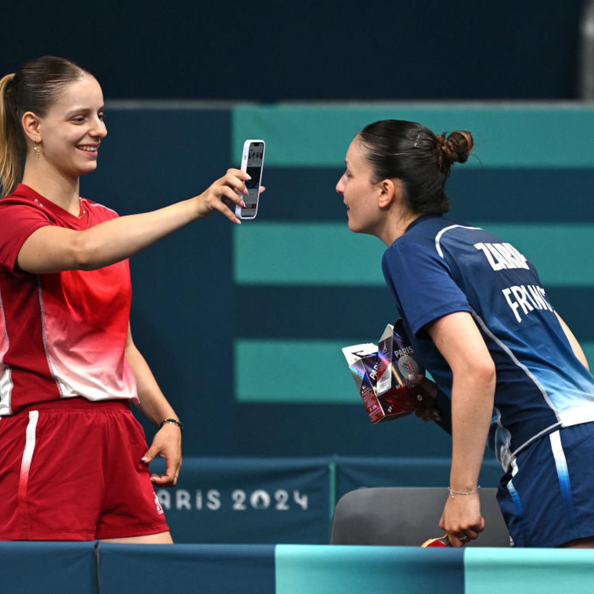 France's table tennis player Charlotte Lutz (left) shows her phone to France's table tennis player Audrey Zarif after their training session at South Arena in Paris on July 23, 2024.