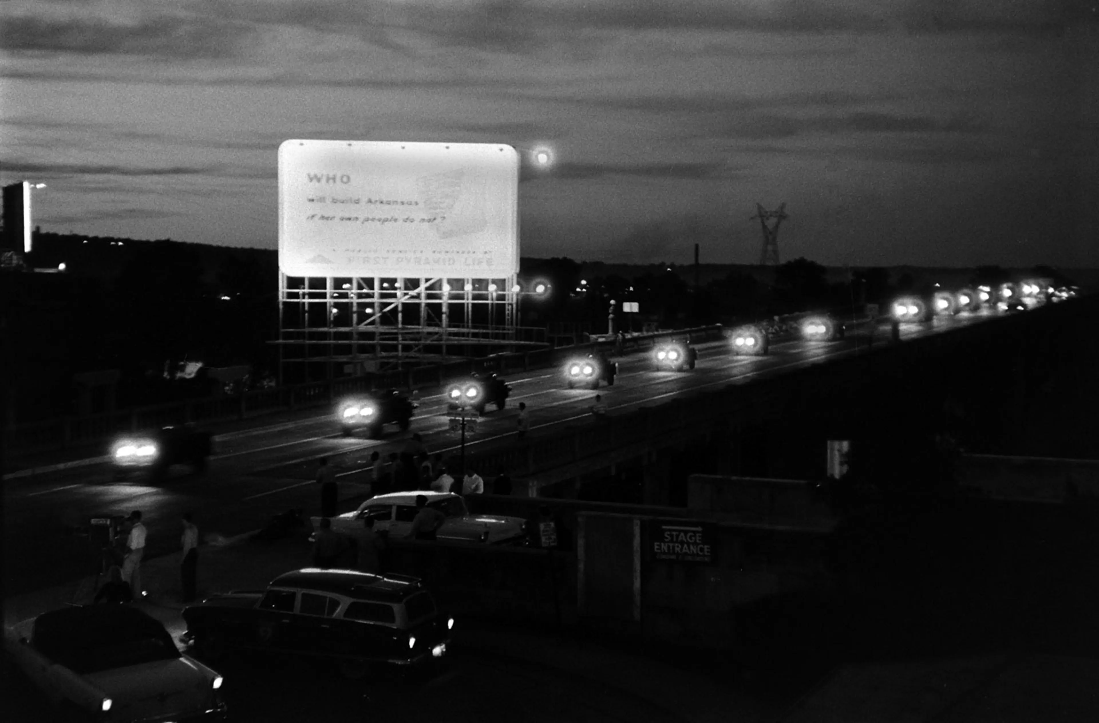 A convoy of Jeeps from the 101st Airborne heads to Little Rock. The billboard they pass reads, "Who will build Arkansas if her own people do not?"