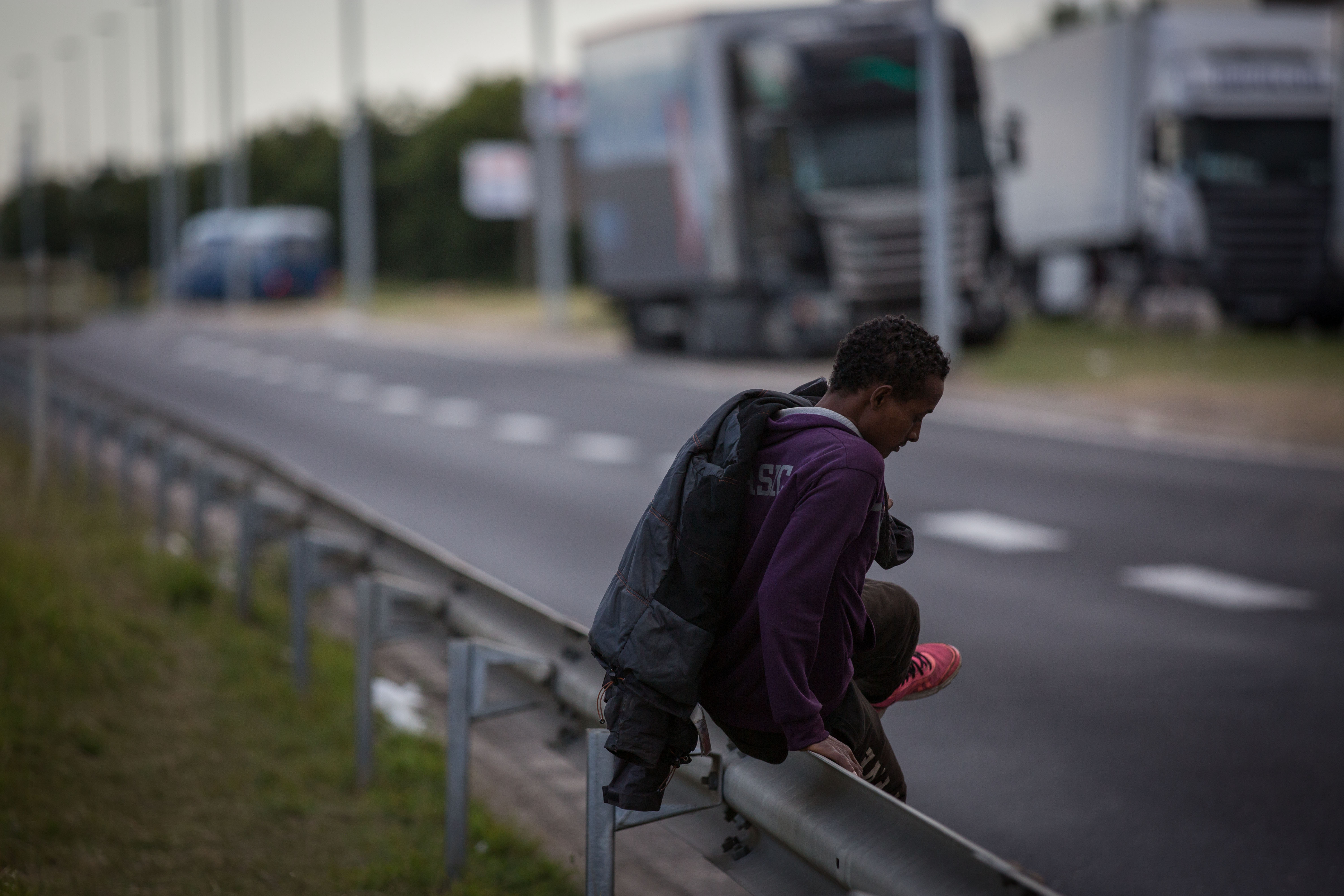 A man climbs a barrier on the side of a road leading to the Eurotunnel terminal in Coquelles on July 30, 2015 in Calais, France.