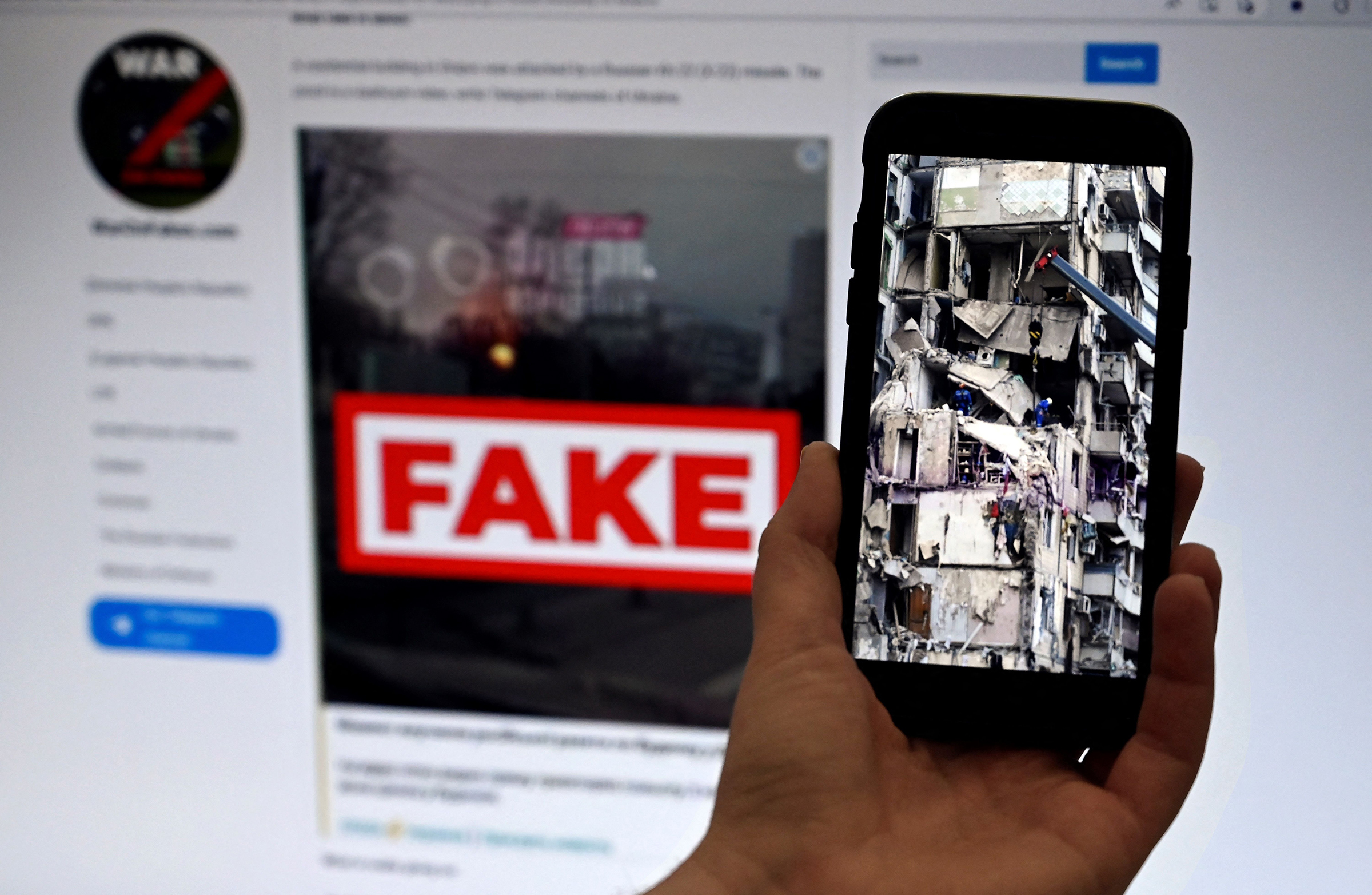 This photo-illustration taken on Feb. 14 shows a phone screen displaying a picture of rescuers working on a residential building destroyed after a missile strike, in Dnipro on Jan. 16, with the WarOnFakes.com website displaying a fake video of the same residential building shown in the background.