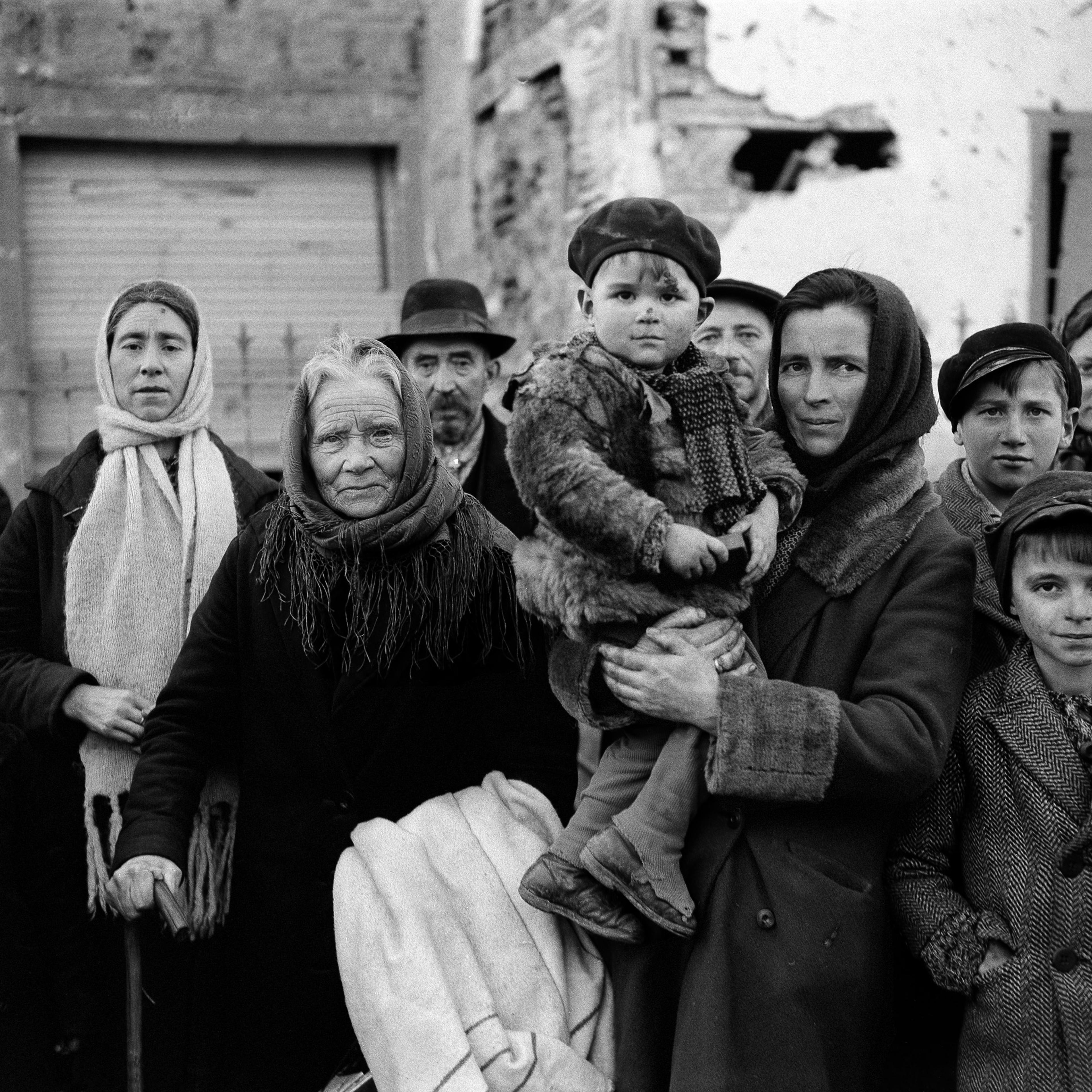 Grim-faced refugees stand in a group on a street in La Gleize, Belgium on Jan. 2, 1945. They are waiting to be transported from the war-torn town after its recapture by American forces during the German thrust into the Belgium-Luxembourg salient.