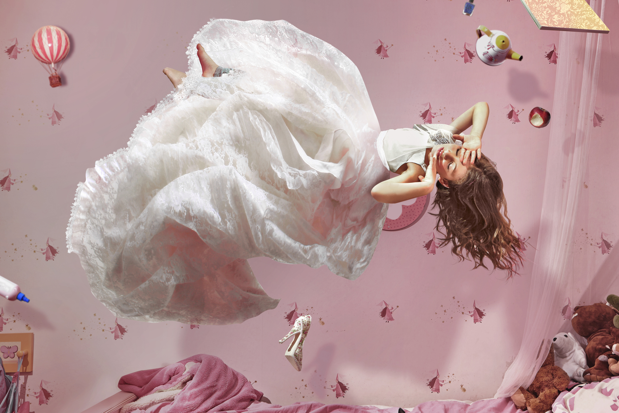 Young girl in long white dress floating in bedroom