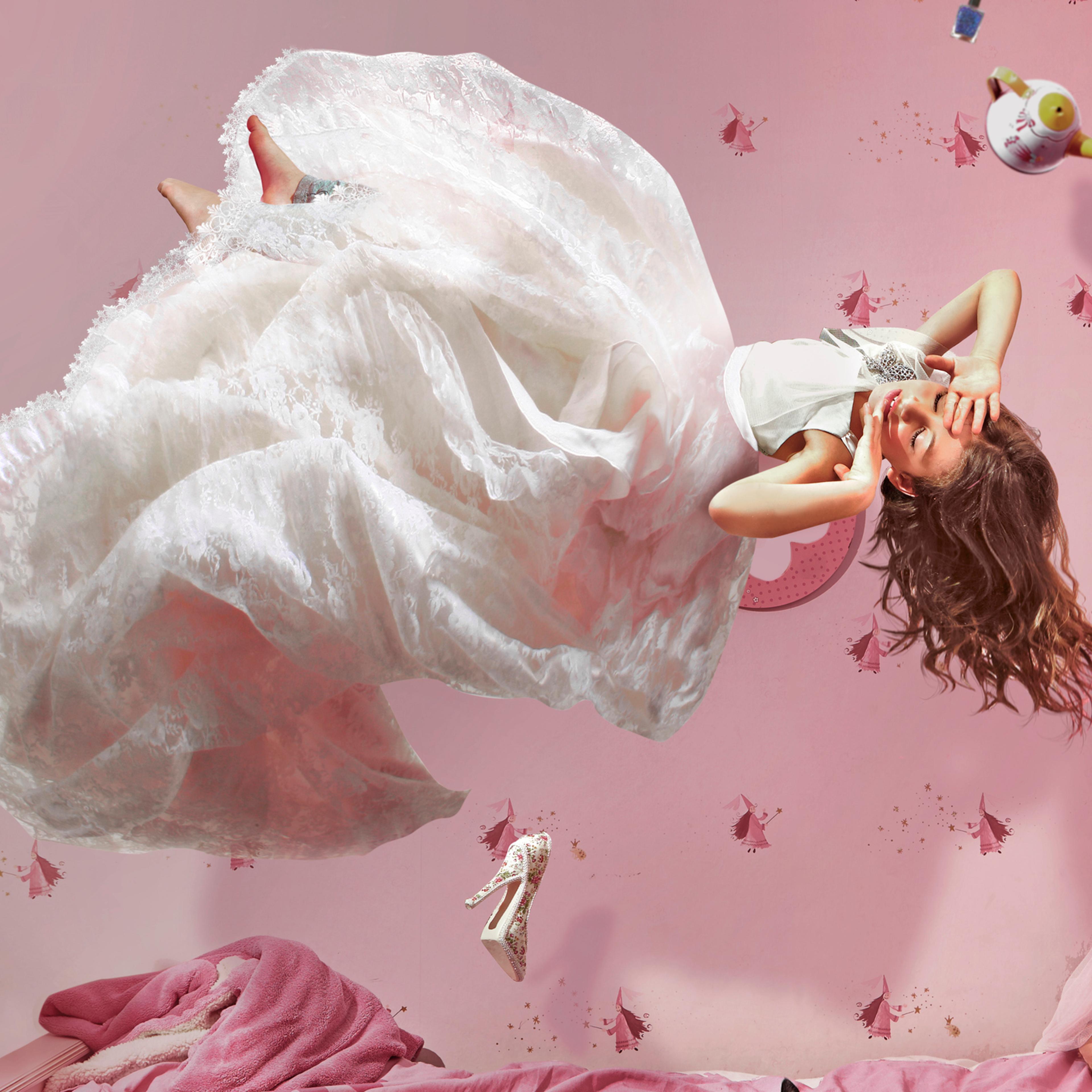 Young girl in long white dress floating in bedroom